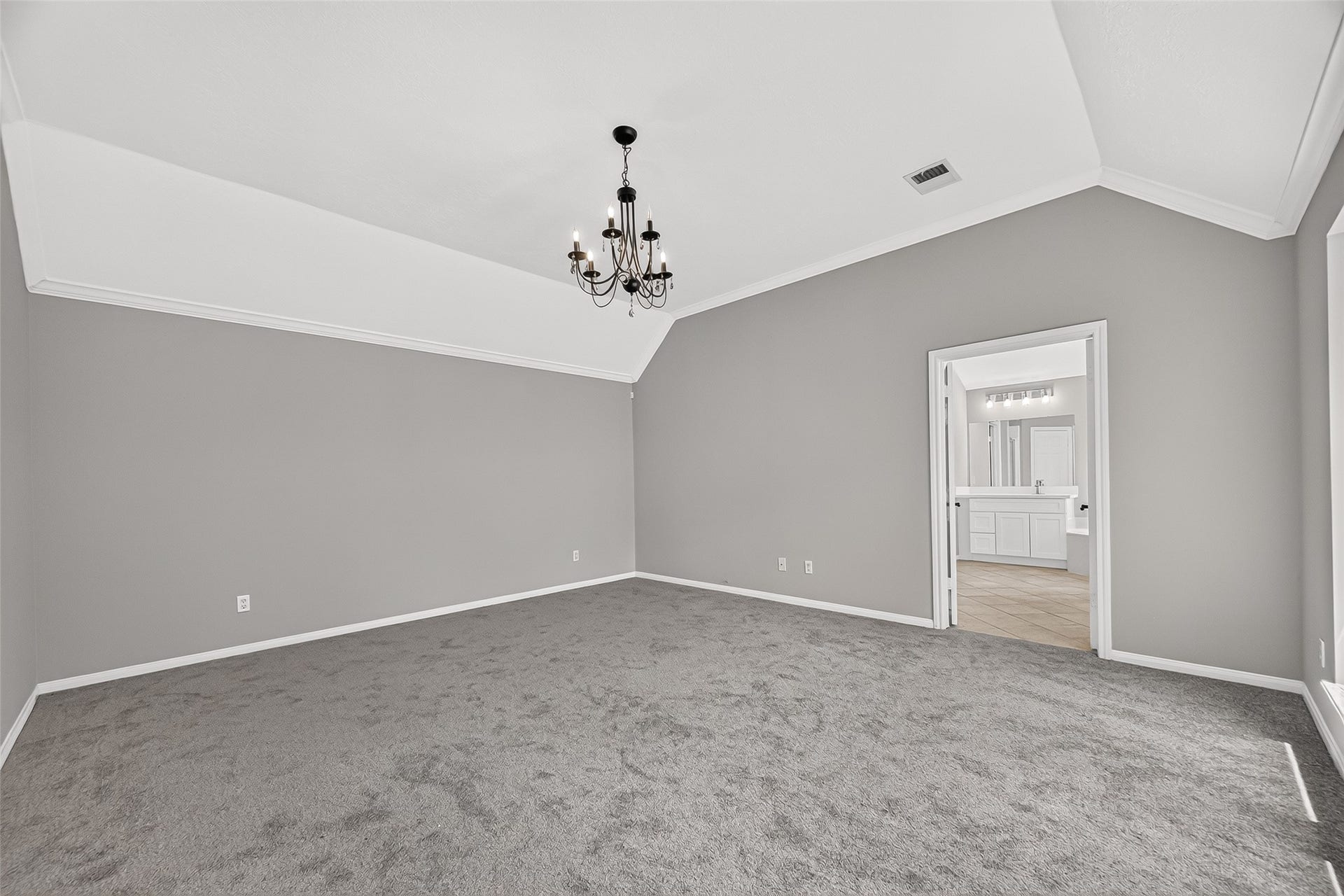 12823 Lady Jane Court, Houston, TX 77044 Spacious bedroom featuring elegant vaulted ceilings, a chic chandelier, and plush carpeting, leading to a bright en-suite bathroom for added privacy and convenience.