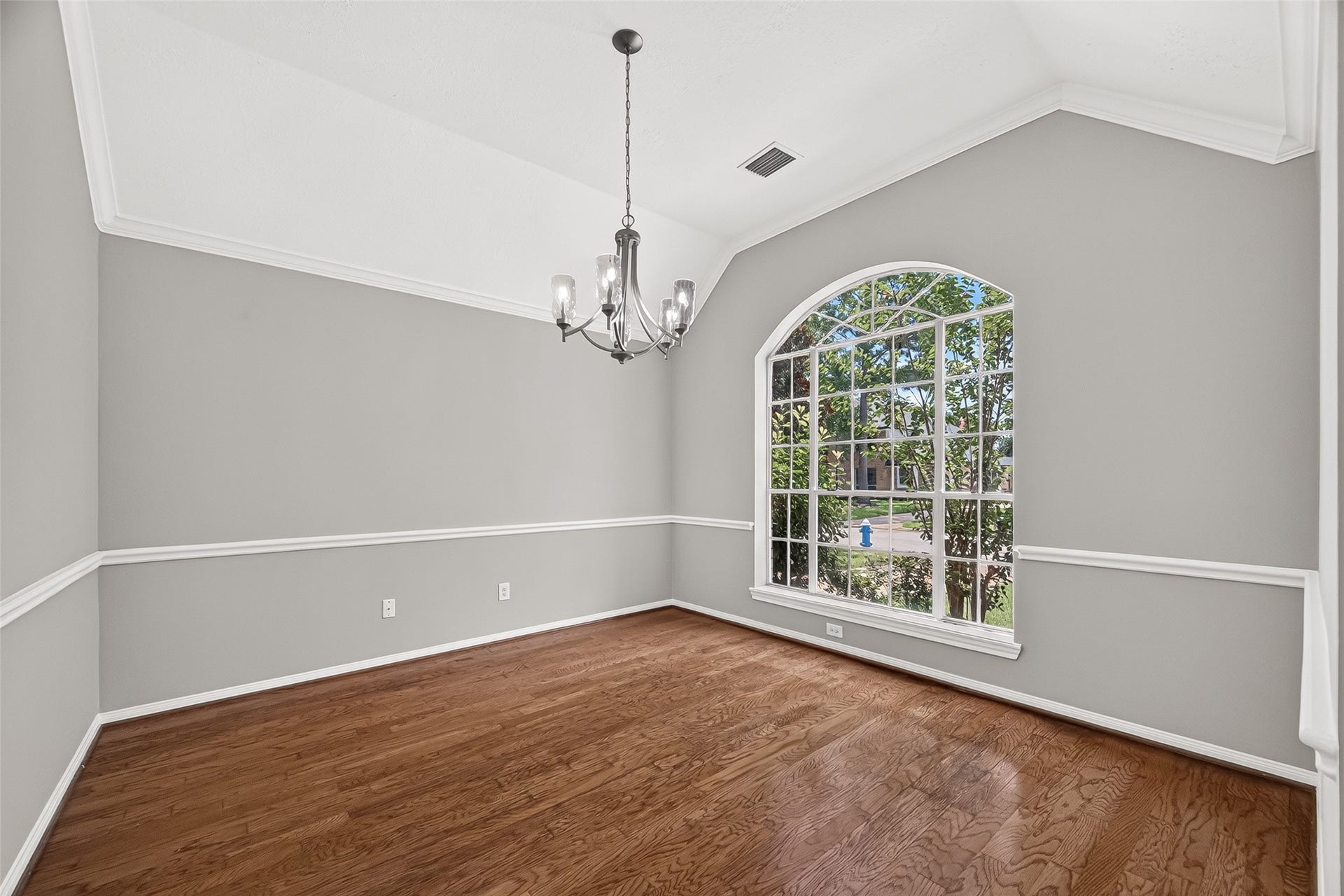 12823 Lady Jane Court, Houston, TX 77044 Elegant dining room featuring large arched windows that invite natural light, complemented by wood flooring and a stylish chandelier.
