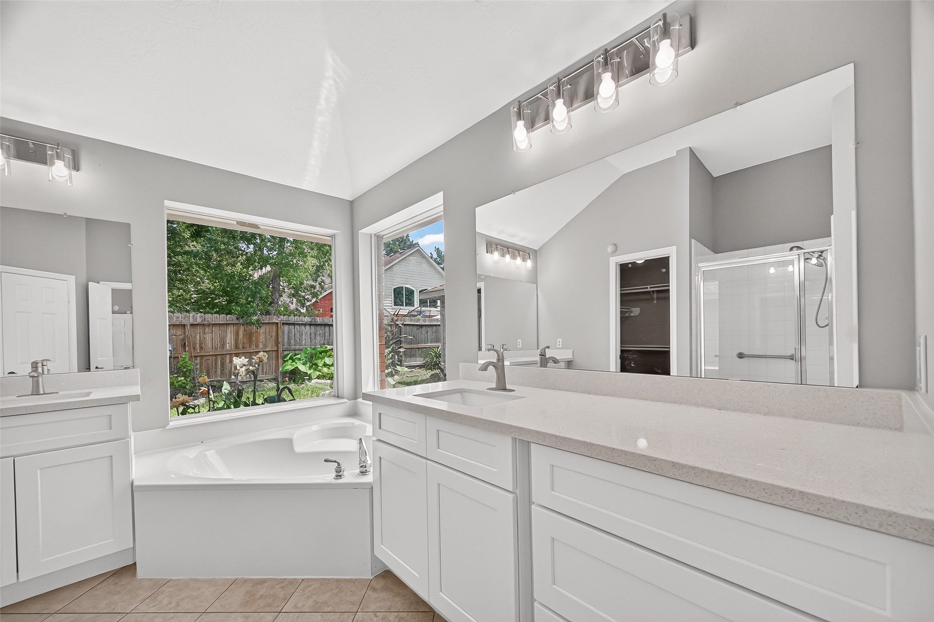12823 Lady Jane Court, Houston, TX 77044 Bright and spacious bathroom featuring double vanities with sleek countertops, a luxurious corner bathtub, and a separate glass-enclosed shower, all enhanced by large windows providing ample natural light.