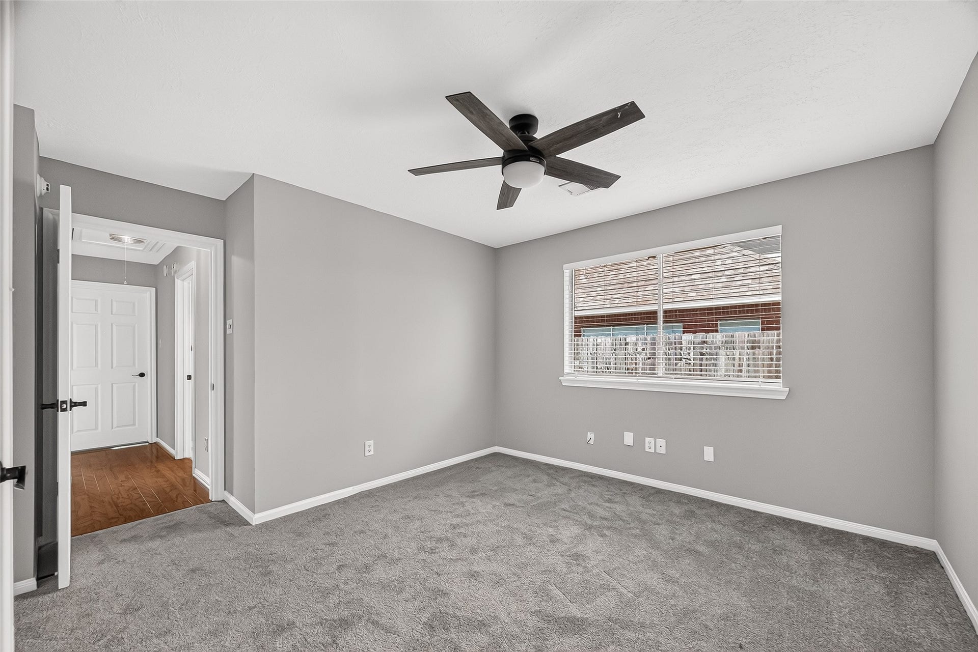 12823 Lady Jane Court, Houston, TX 77044 Spacious bedroom with neutral gray walls, plush carpet, and a modern ceiling fan, complemented by a large window for natural light.