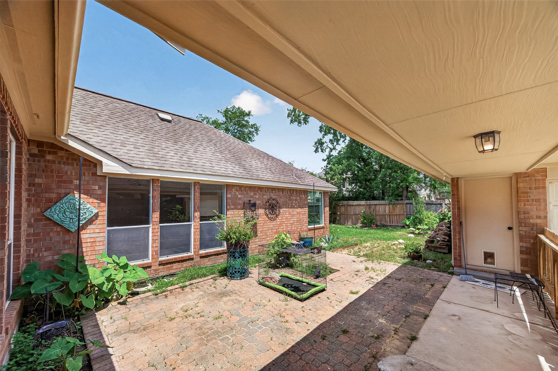 12823 Lady Jane Court, Houston, TX 77044 Backyard patio with a mix of brick and stone paving, surrounded by lush greenery and a privacy fence, perfect for outdoor relaxation and entertaining.