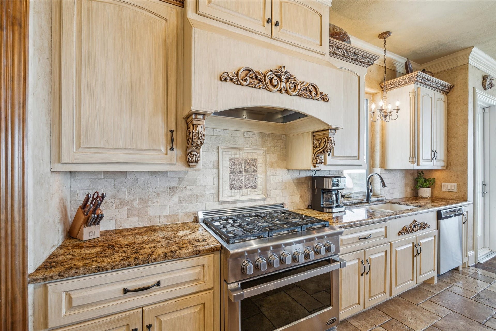 9 Happy Jack, Hitchcock, TX 77563 At the heart of the space is a DCS 6-burner gas range and convection oven, set against a backdrop of warm, tumbled stone backsplash tiles and custom mosaic tiled design. Above the range, a stunning custom wood range hood takes center stage, adorned with intricate carved scrollwork and corbels that echo Old World design influences.