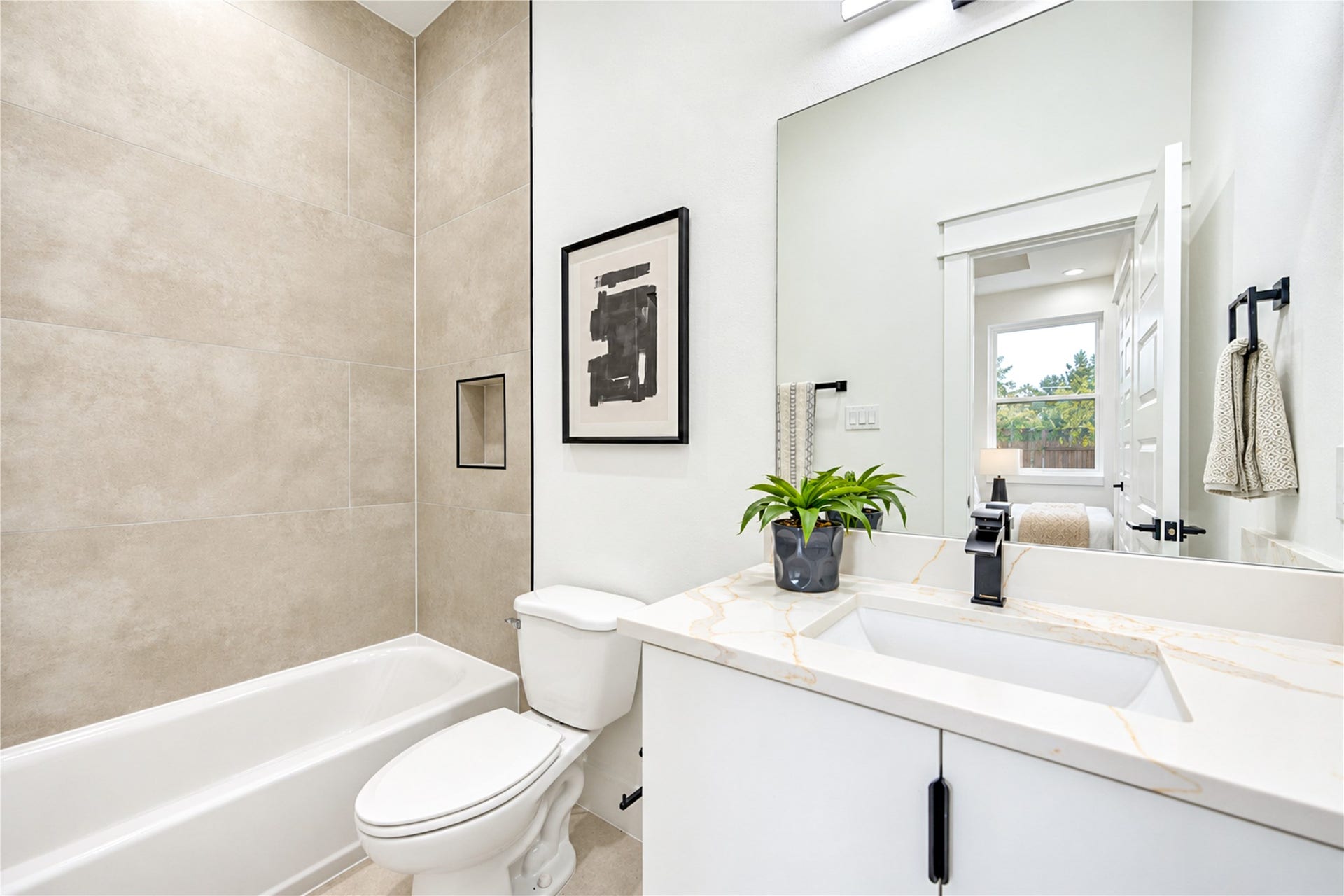 Convenient first-floor ensuite full bath showcasing a modern single vanity with quartz counters, sleek matte black hardware, and a tub/shower combo with large-format neutral tile.