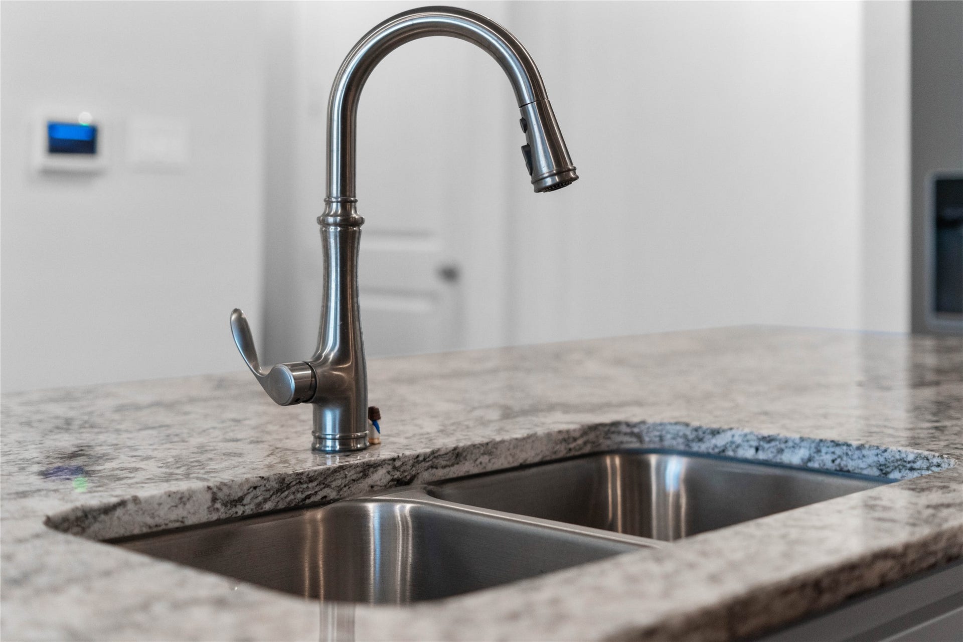 The kitchen island features an undermount double-basin stainless steel sink paired with a premium brushed nickel gooseneck faucet, offering an integrated pull-down sprayer for maximum culinary convenience.