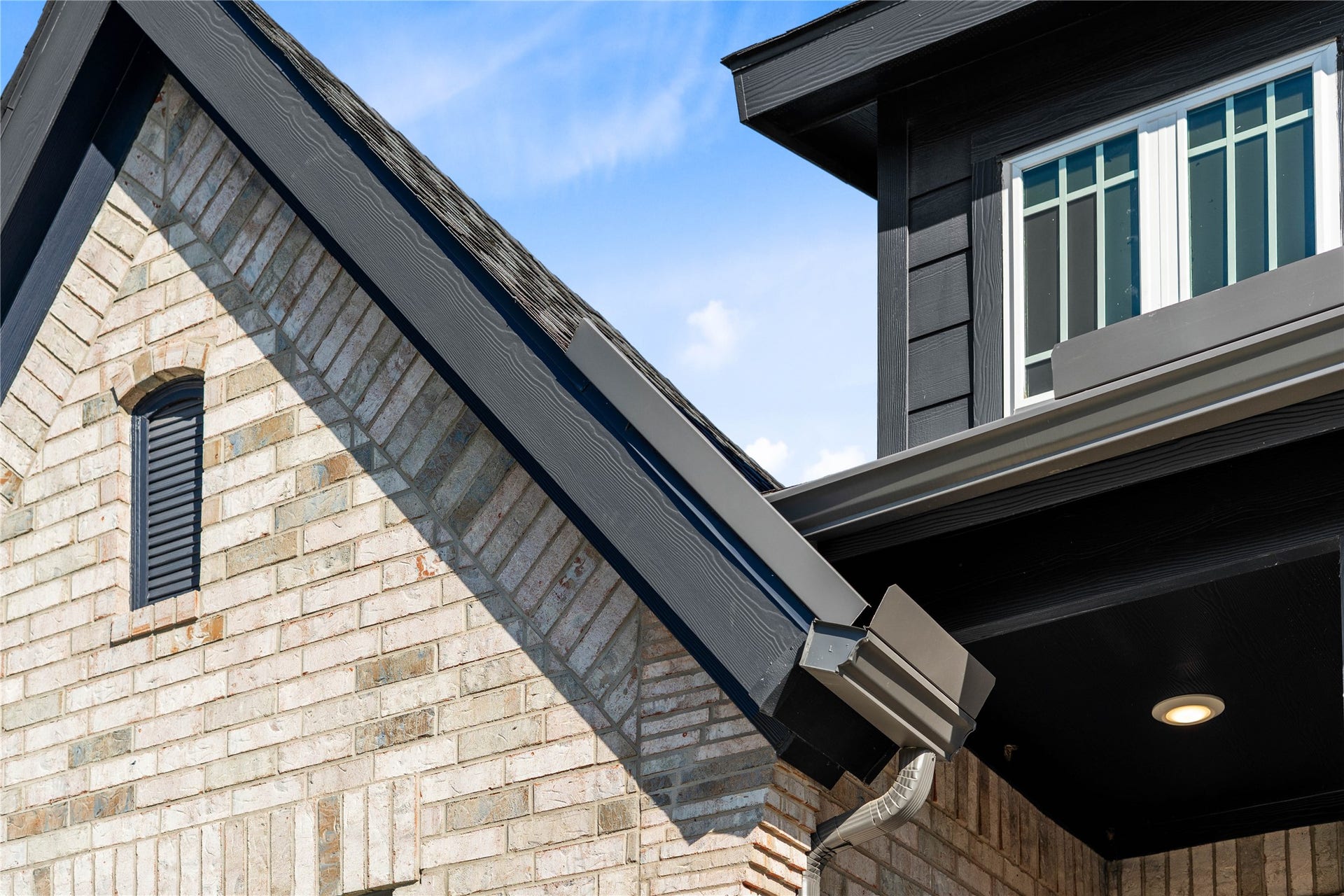 A detailed look at the home's exterior craftsmanship, showcasing the intricate brickwork accents, contrasting dark trim, integrated seamless gutters, and a prominent dormer window that maximizes natural light.