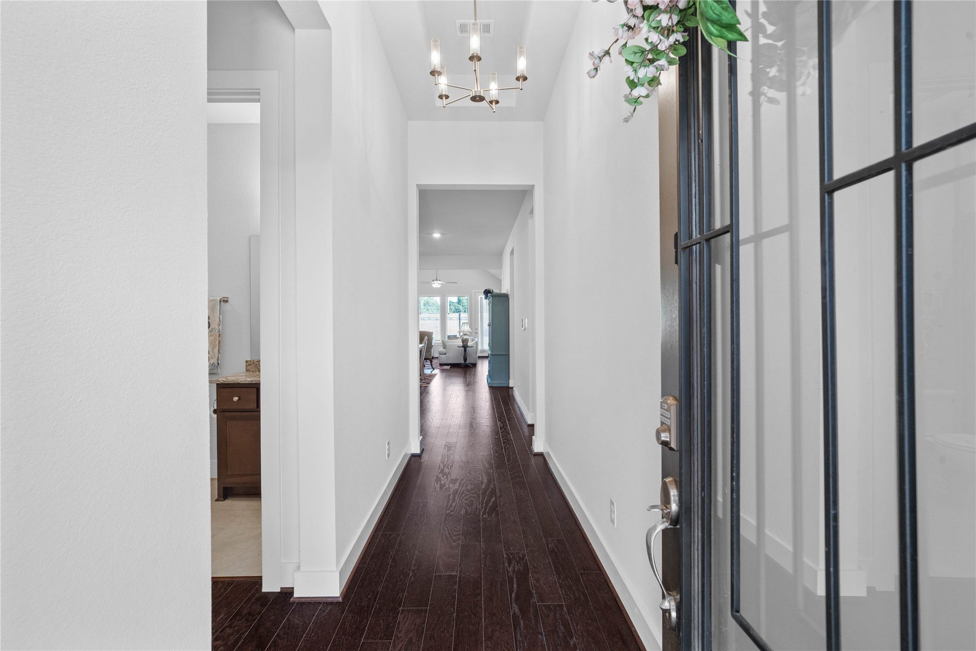 A welcoming foyer introduces the home's bright and airy interior, showcasing rich dark wood floors, crisp neutral walls, a recessed ceiling accent with a modern light fixture, and an open sightline leading directly into the main living area.