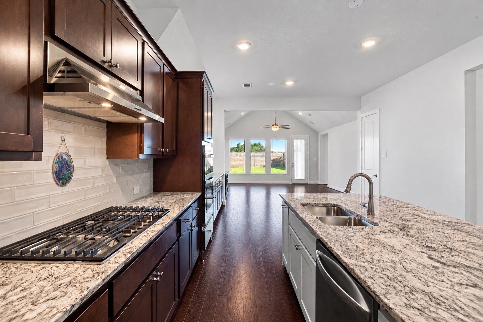 Designed for the modern home chef, this beautifully appointed workspace features a premium stainless steel gas cooktop with a matching vent hood, an elegant glossy subway tile backsplash, and extensive granite counter space that anchors the open-concept layout.