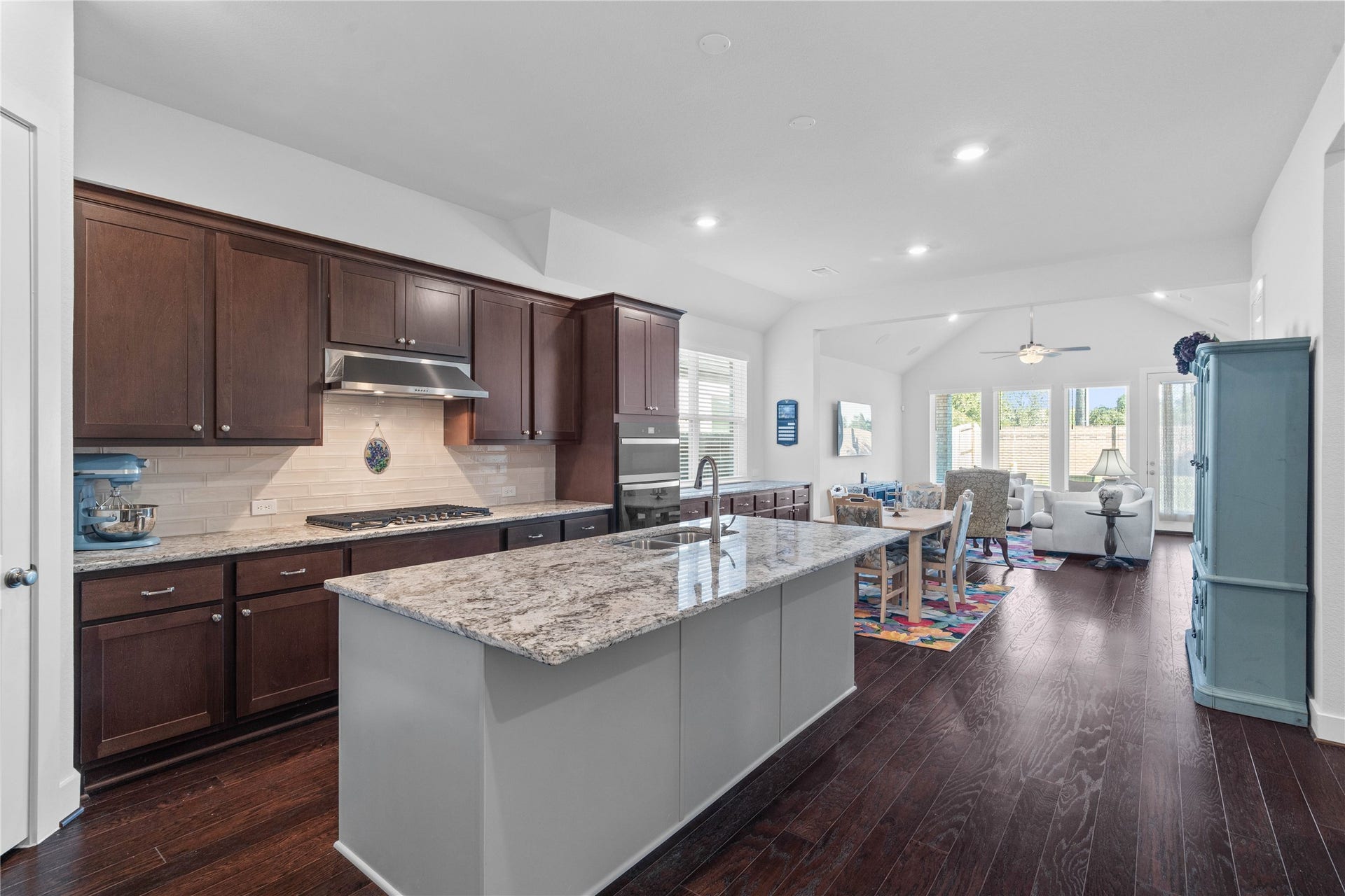 The chefs kitchen serves as the heart of the home, featuring rich dark cabinetry, built-in stainless steel appliances, a modern backsplash, and a spacious center island with a granite countertop that flows seamlessly into the open-concept dining and living areas.