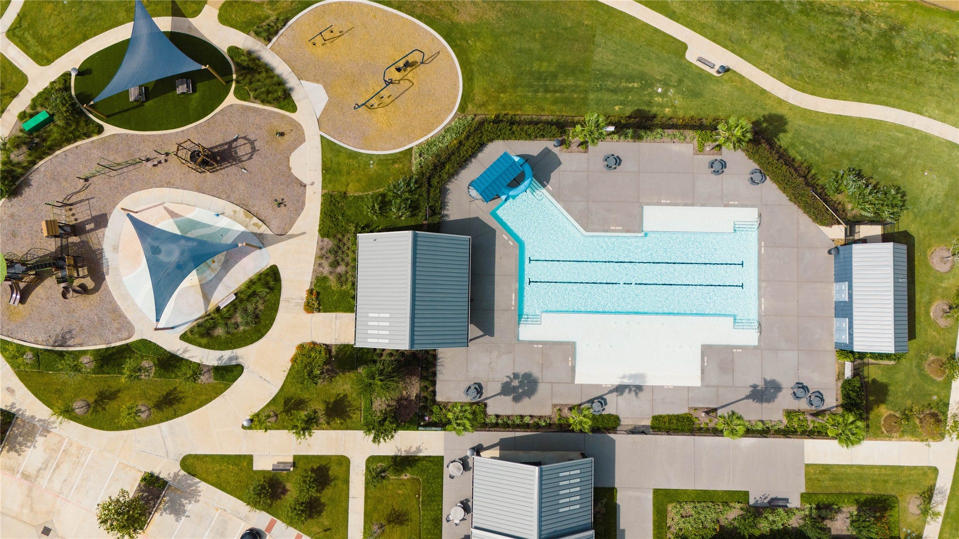 An aerial view of the resort-style Pecan Ridge community amenities, showcasing a sprawling swimming pool with lap lanes and a waterslide, a private clubhouse facility, and multiple expansive shade-covered playground zones connected by walking paths.