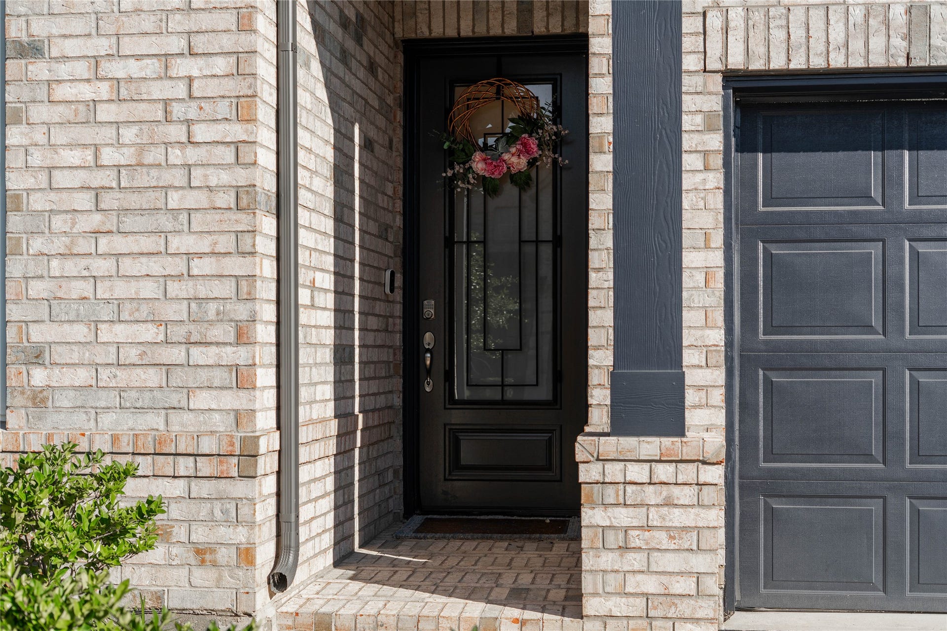 The inviting front entryway features an elegant, dark-trimmed front door with inset privacy glass, framed by classic light brickwork, and an accent brick porch floor.