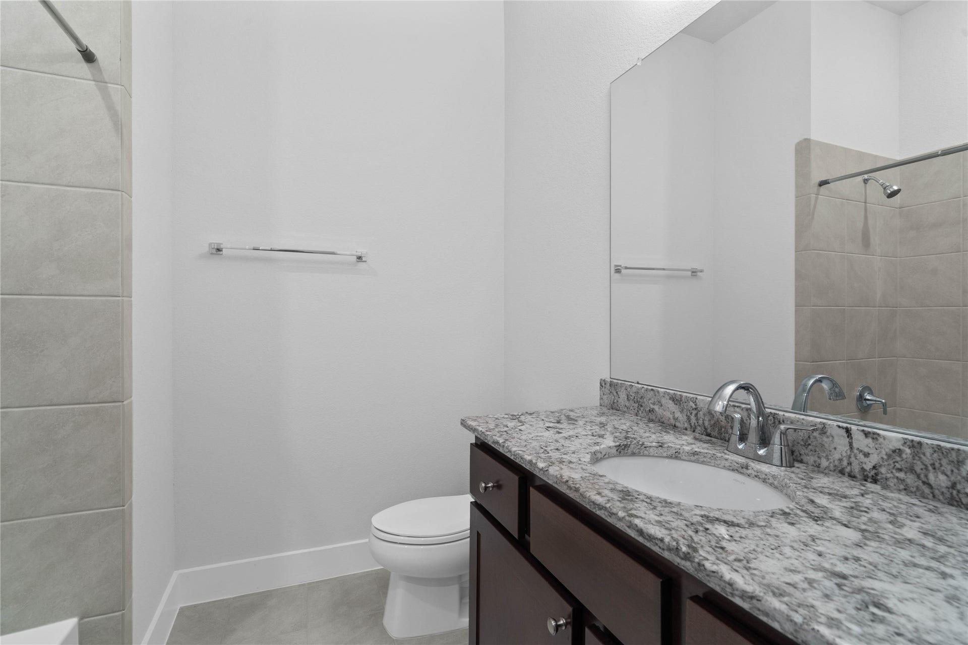 The second full bathroom offers a matching high-end finish, featuring a beautiful granite vanity top, dark wood cabinetry, clean tile floors, and a pristine tub/shower combination.