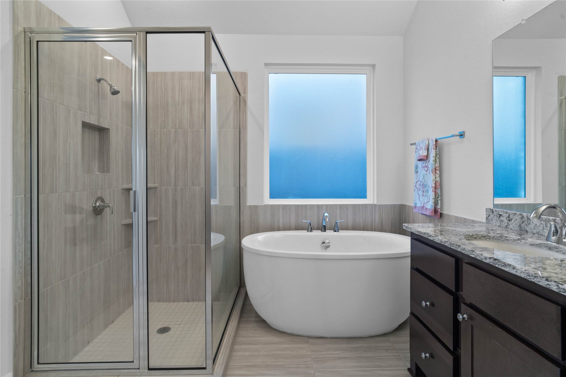 A closer look at the spa-inspired amenities, highlighting the deep freestanding soaking tub positioned beneath a large frosted privacy window, alongside a separate glass-enclosed walk-in shower complete with floor-to-ceiling tile work and an integrated storage niche.