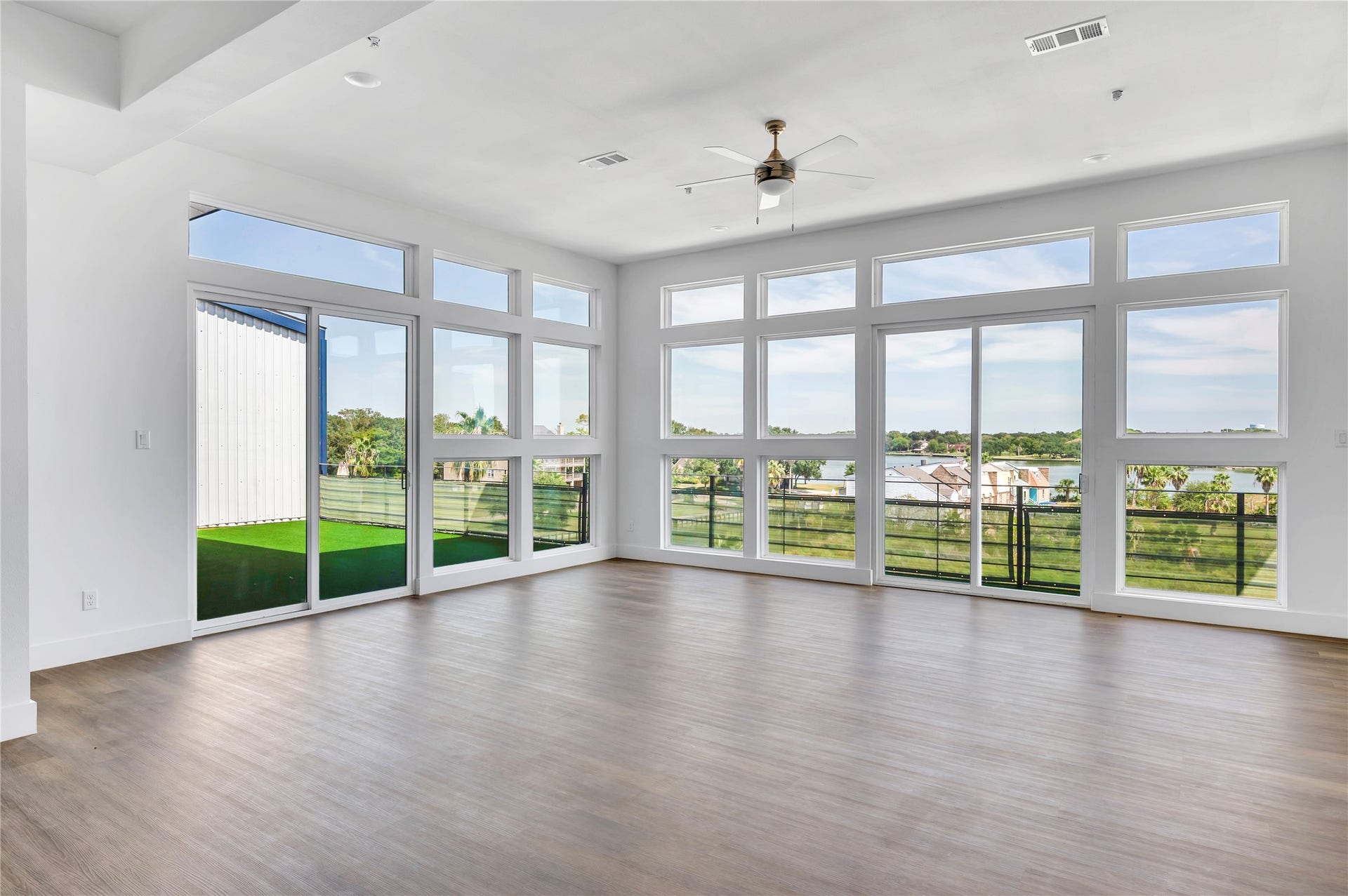 119 Kirby Road, #5304, Taylor Lake Village, TX 77586 Spacious, sunlit room with expansive windows offering stunning views and access to a balcony, featuring elegant wood flooring and a modern ceiling fan.