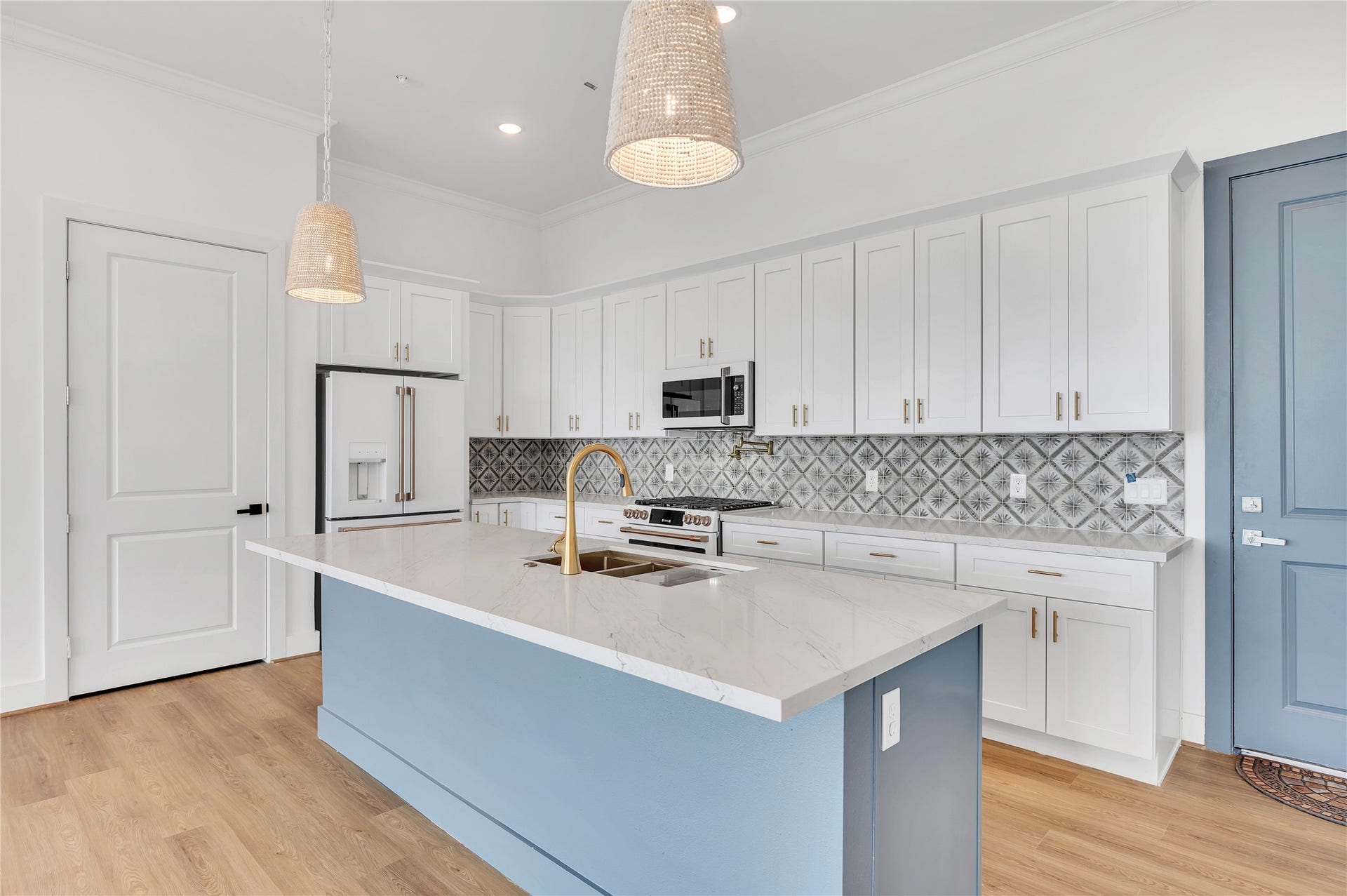 119 Kirby Road, #5304, Taylor Lake Village, TX 77586 Bright and modern kitchen featuring sleek white cabinetry, a stunning marble island with a gold faucet, and elegant pendant lighting. The patterned backsplash adds a touch of sophistication, perfectly complementing the polished wood flooring.