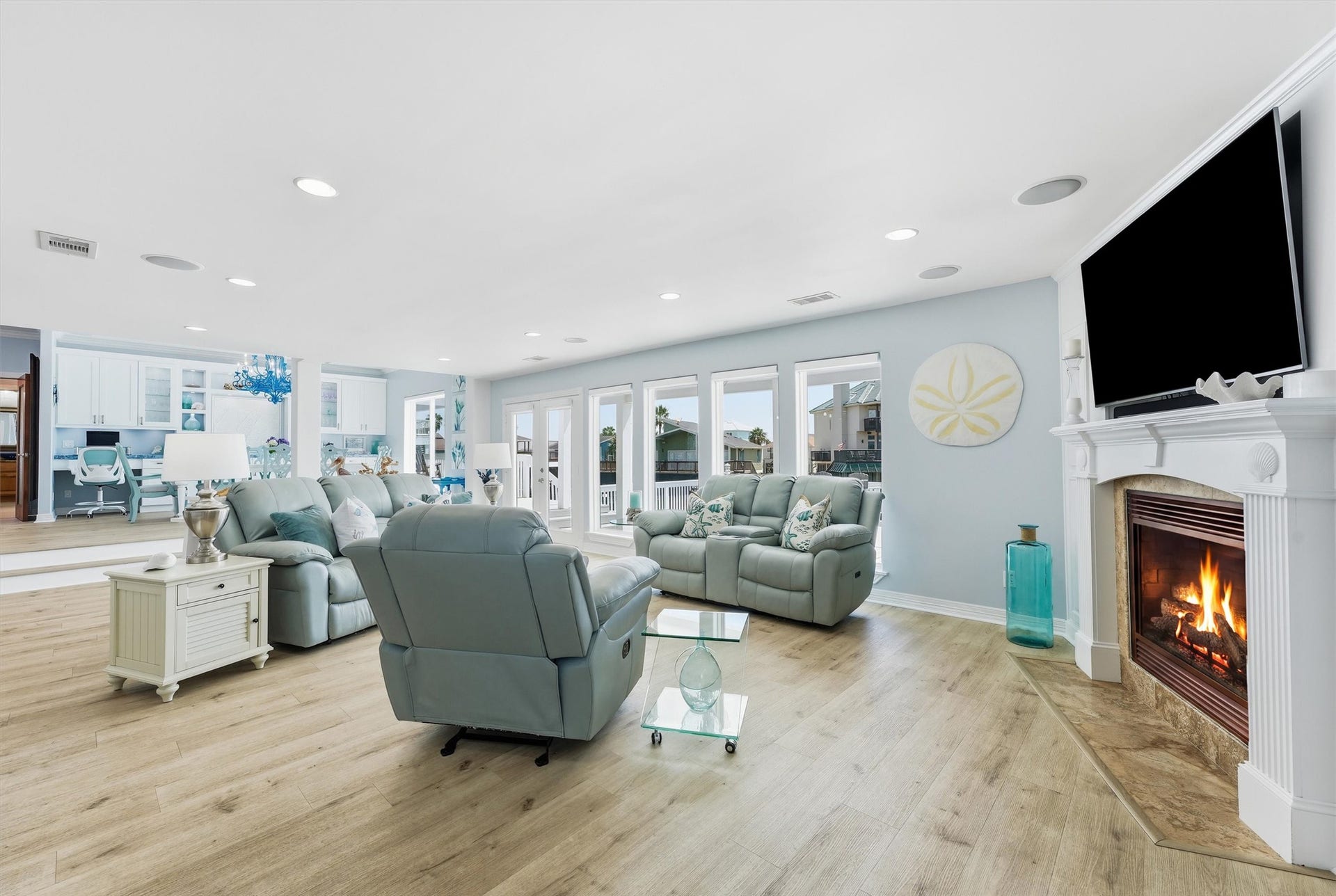 Spacious waterfront living room with a fireplace, abundant natural light, and a wall of windows overlooking the canal.