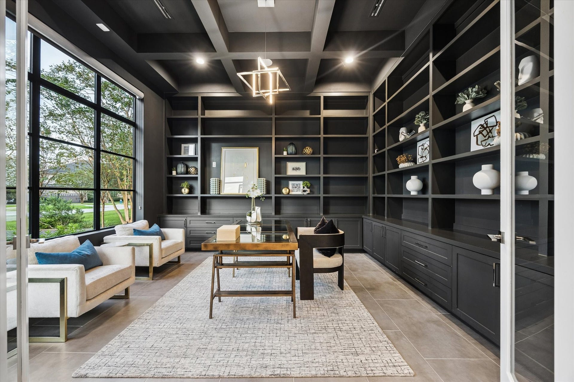 10943 Britoak Lane, Houston, TX 77079 Sophisticated private study featuring custom floor-to-ceiling built-ins, a coffered ceiling, designer lighting, and expansive windows overlooking lush greenery.