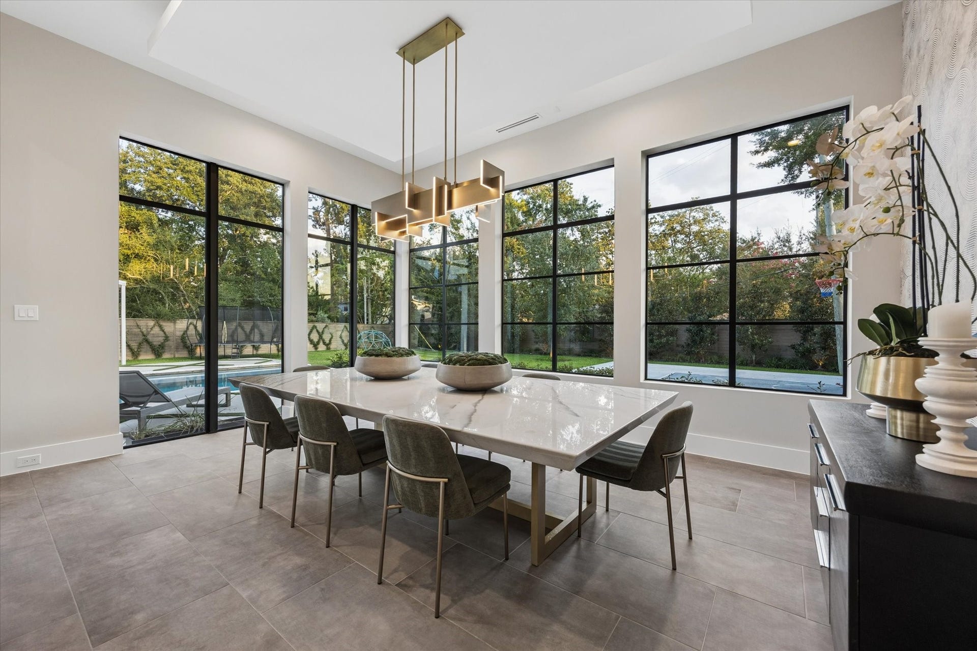 10943 Britoak Lane, Houston, TX 77079 Refined dining area featuring expansive windows, a statement chandelier, and beautiful views of the lush backyard and pool.