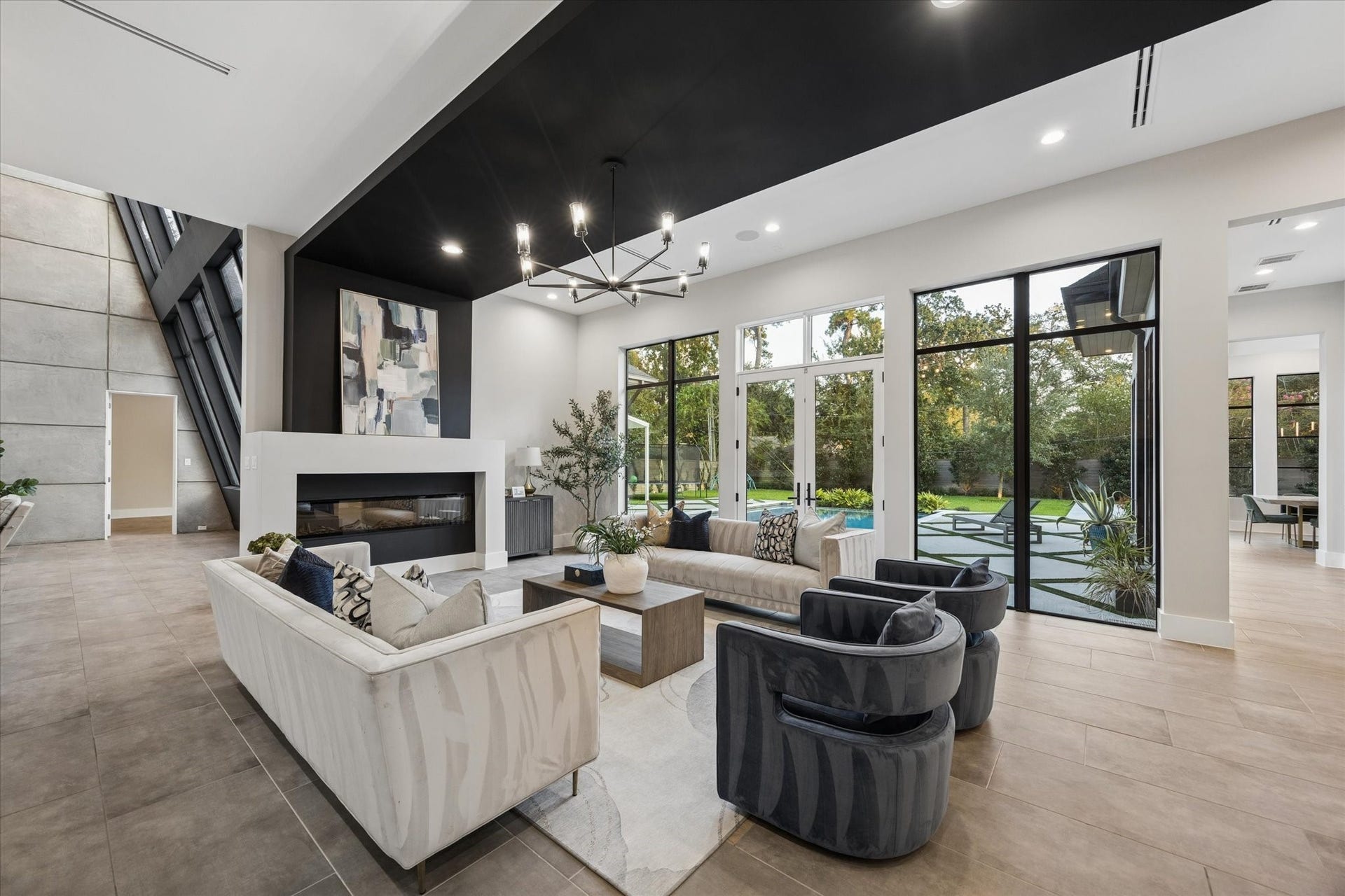 10943 Britoak Lane, Houston, TX 77079 Expansive living room featuring a sleek modern fireplace, dramatic ceiling detail, and floor-to-ceiling windows overlooking the lush backyard.