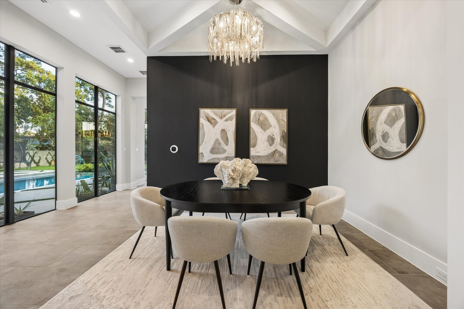 10943 Britoak Lane, Houston, TX 77079 Elegant dining area featuring a dramatic black accent wall, a statement chandelier, and expansive windows that fill the space with natural light and overlook the pool.