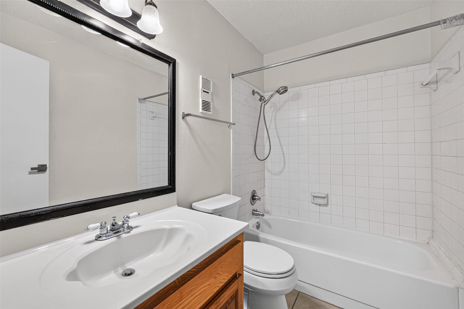 Secondary full bathroom featuring a tub/shower combination, spacious vanity, and large framed mirror.