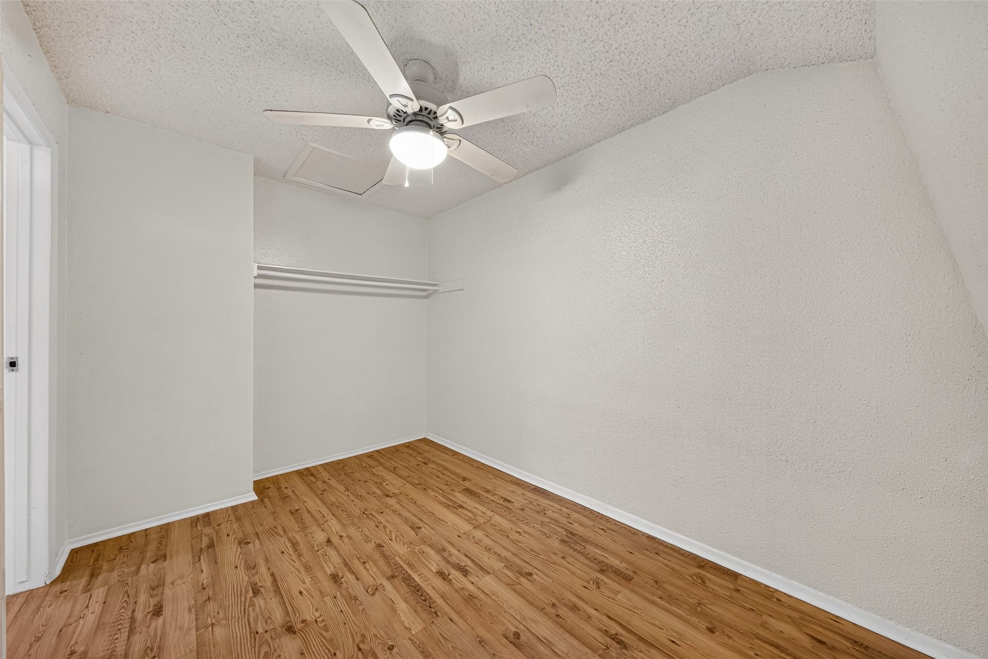 Versatile upstairs flex room with wood-look flooring, ceiling fan, and open closet area.