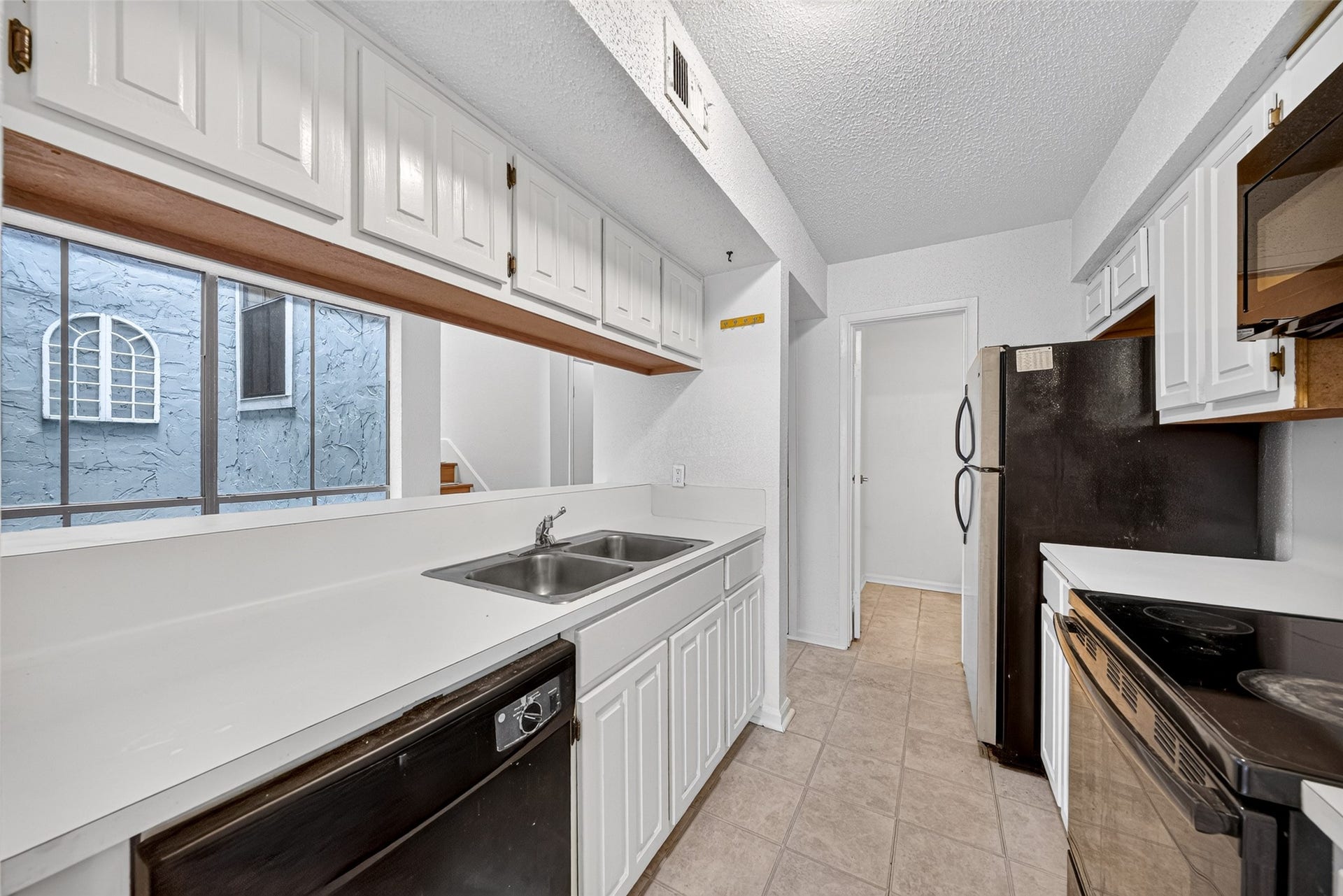 Functional kitchen featuring white cabinetry, breakfast bar, double-basin sink, and black appliances.