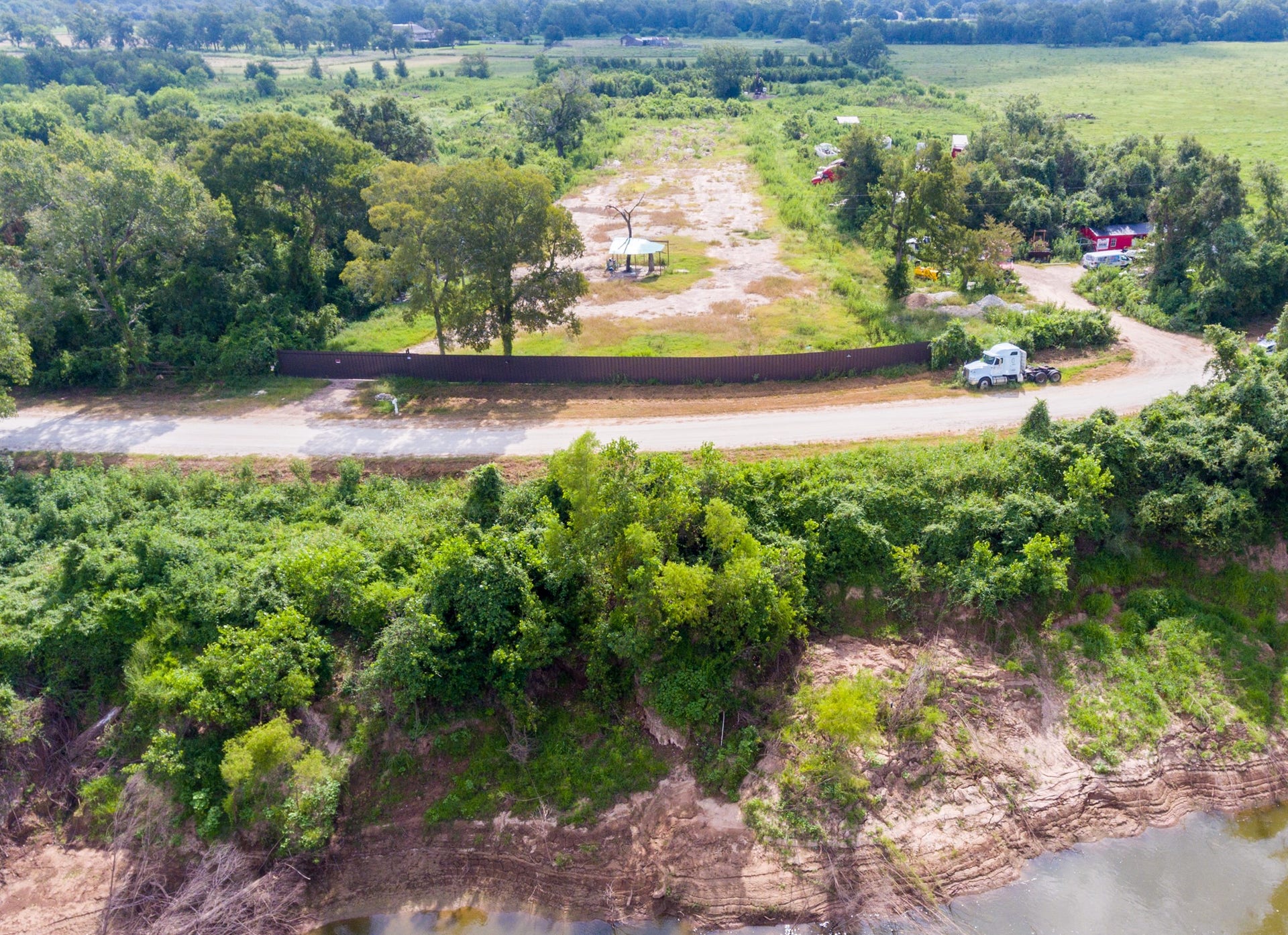 Expansive, partially cleared land with lush greenery and a dirt road. A truck is visible, and the area offers privacy with trees and potential river views. Ideal for development or a secluded home site.