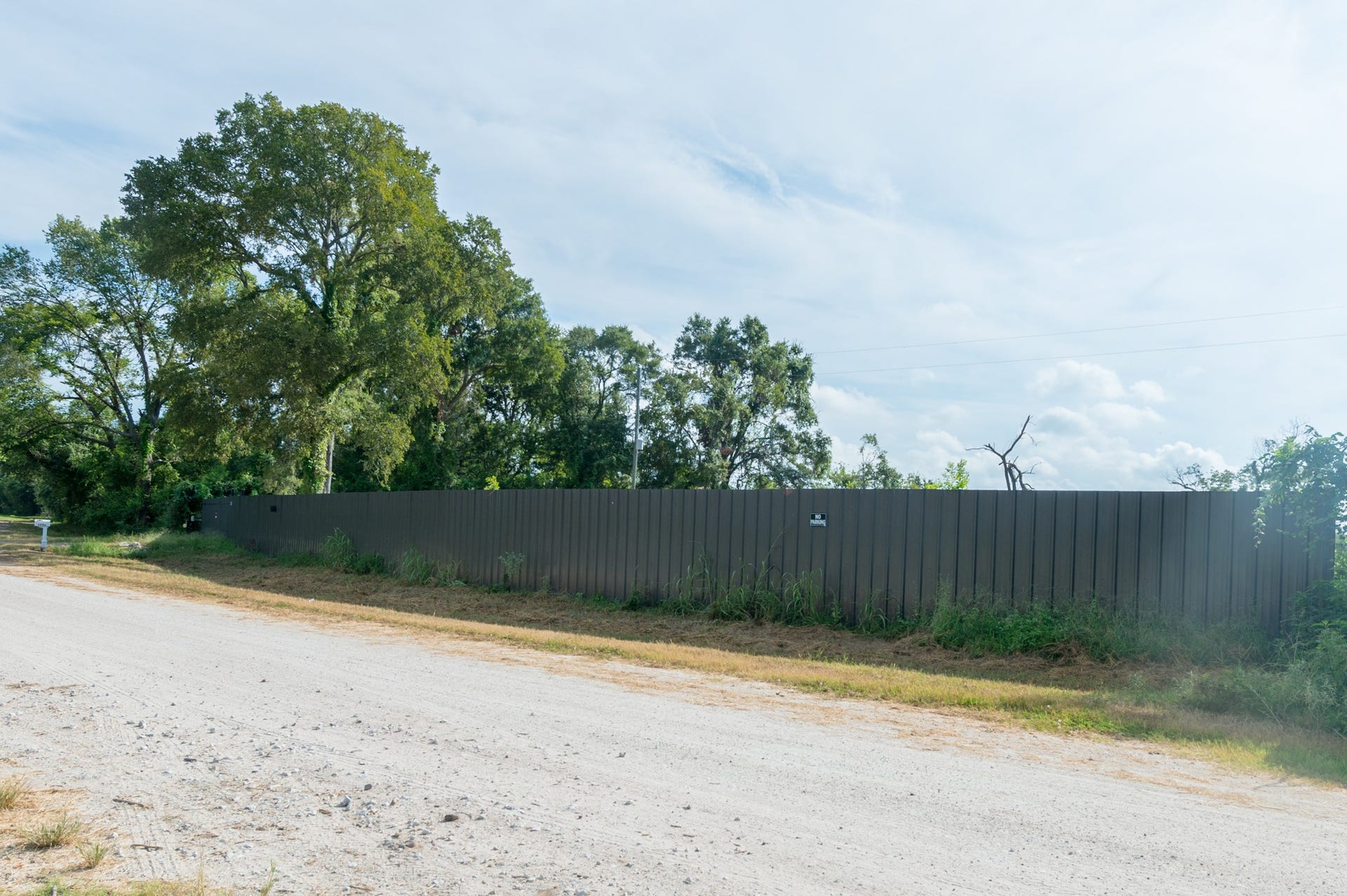 A long metal fence lines a dirt road, bordered by lush trees and greenery, providing privacy and a natural backdrop.