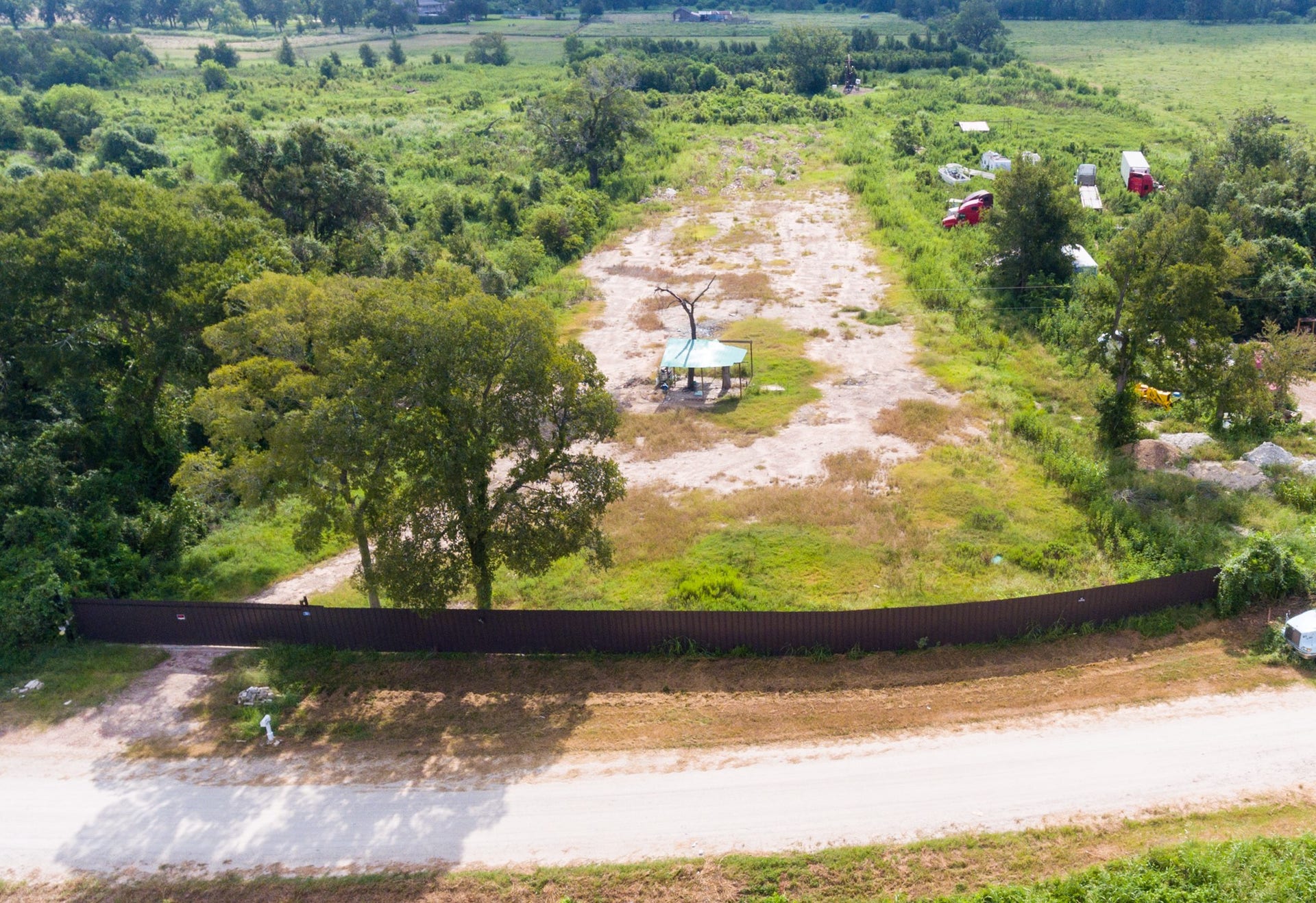 This photo shows a large, open plot of land surrounded by greenery, with a few scattered trees and a fence at the front. It's a secluded area, ideal for development, offering ample space and scenic views.