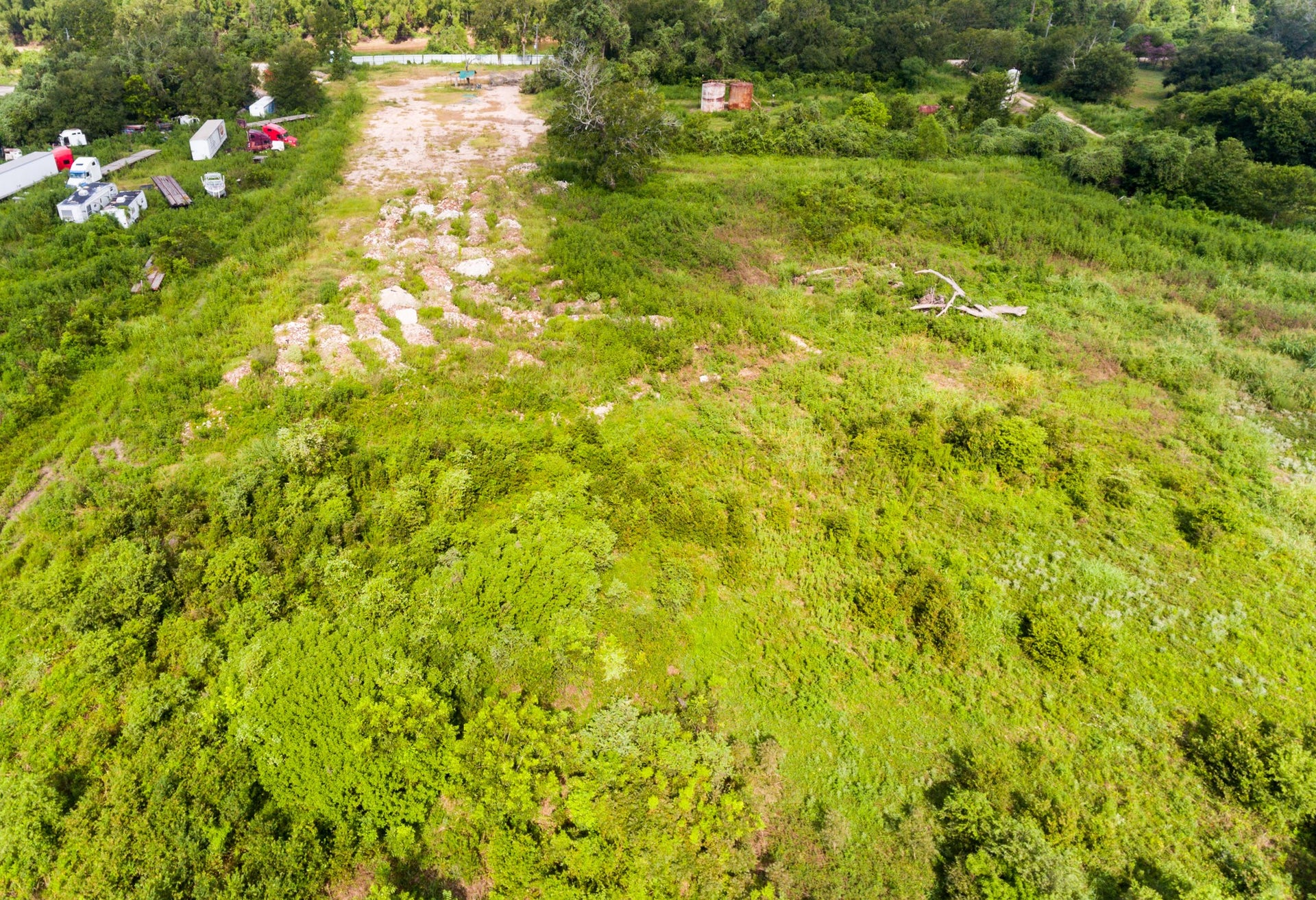 This aerial photo showcases a large, lush green plot of land with scattered trees and open areas. It includes some parked vehicles and trailers, indicating possible utility access. Ideal for development or recreational use, the surroundings offer a serene, natural setting.