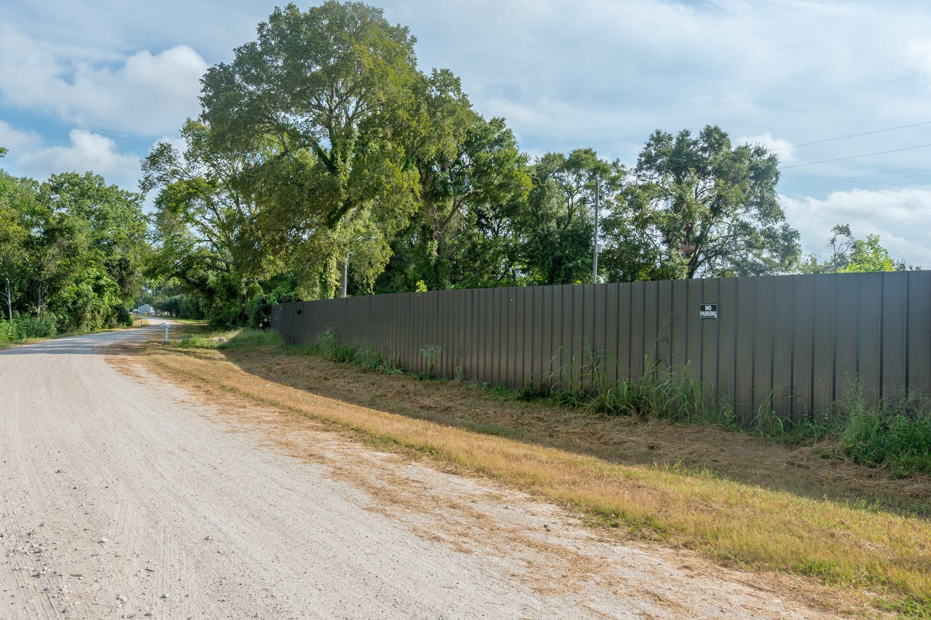 A peaceful, rural setting with a dirt road lined by lush trees and a long metal fence, offering privacy and a natural ambiance.