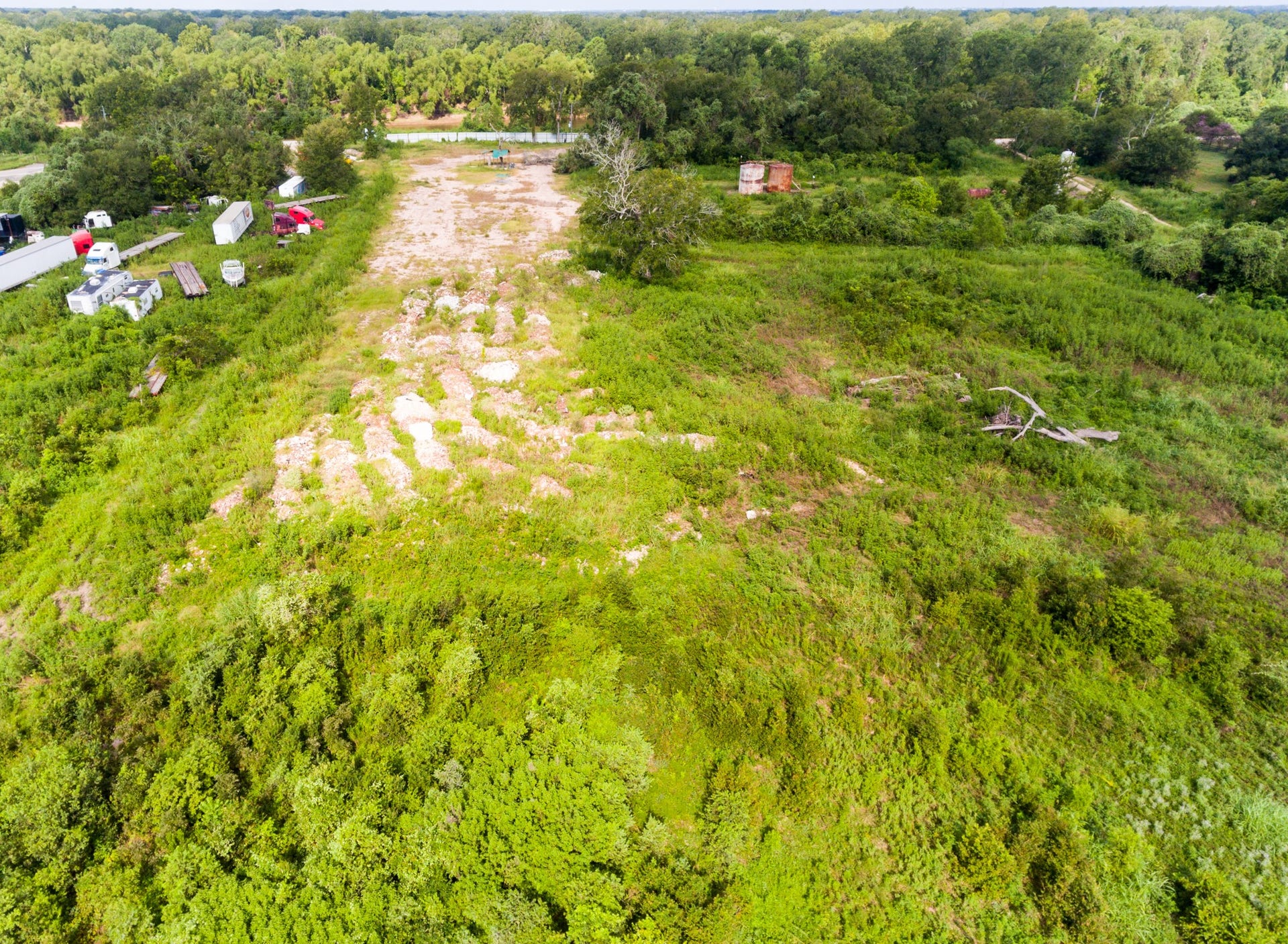 This photo shows a large, open plot of land surrounded by lush greenery, with a partially cleared area and some vehicles and equipment visible. It's ideal for development with serene, wooded surroundings.