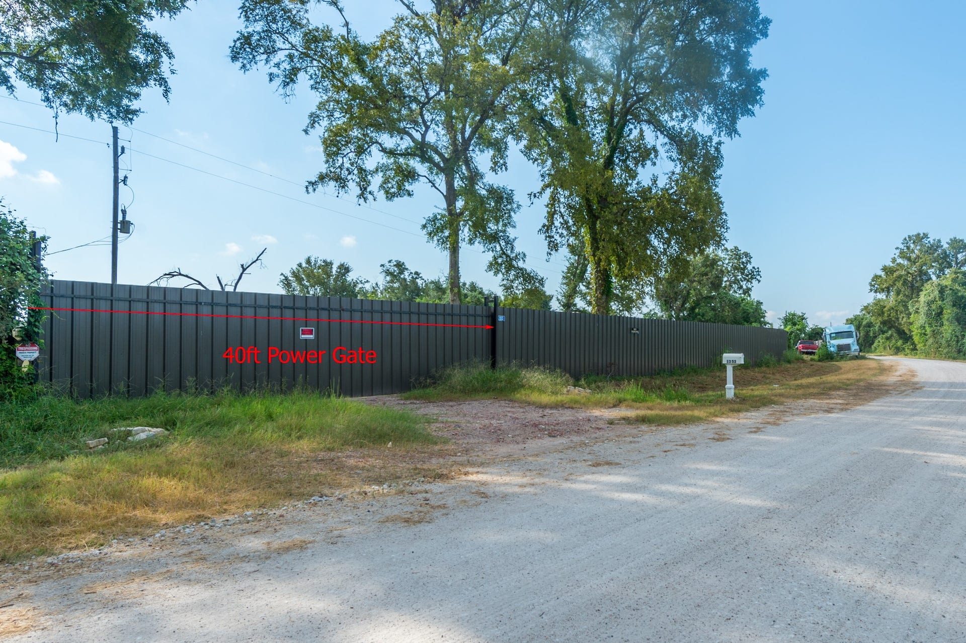 This image shows a rural property with a 40-foot power gate along a gravel road. The area is lined with trees, providing a private and secluded feel.
