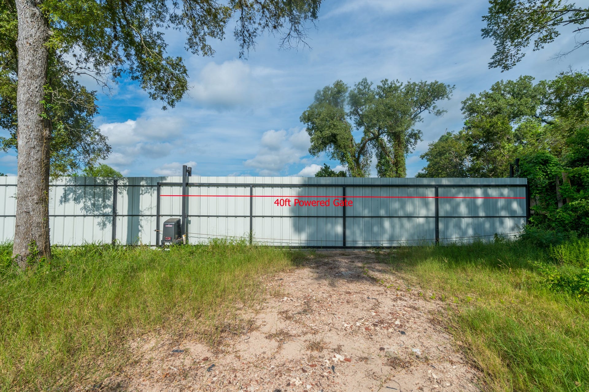A 40-foot powered gate secures this property, surrounded by lush greenery and mature trees, providing privacy and a natural setting.