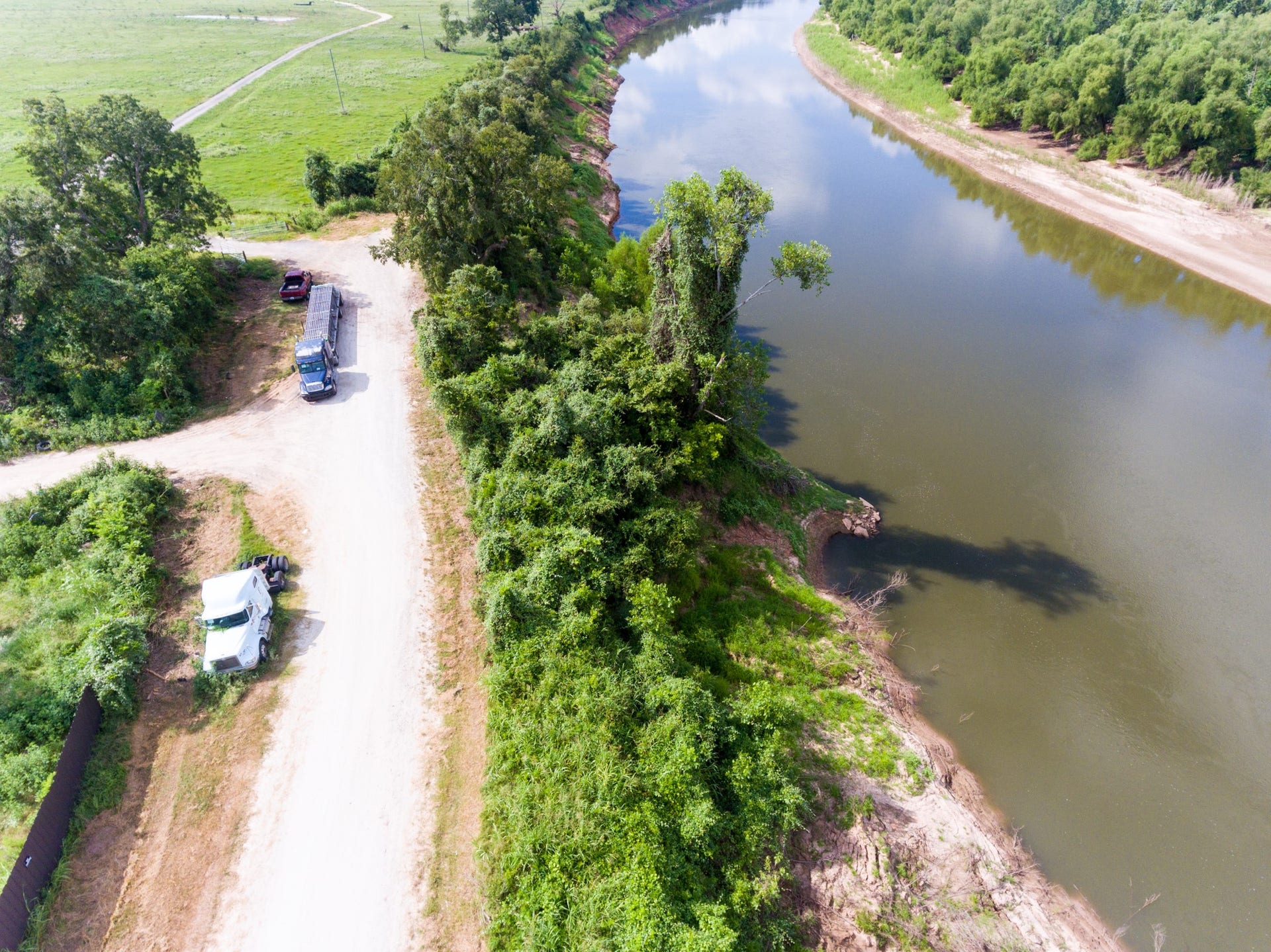 This aerial photo showcases a scenic riverside property with lush greenery and a dirt road, providing a serene and natural setting. Ideal for those seeking tranquility and a connection to nature.
