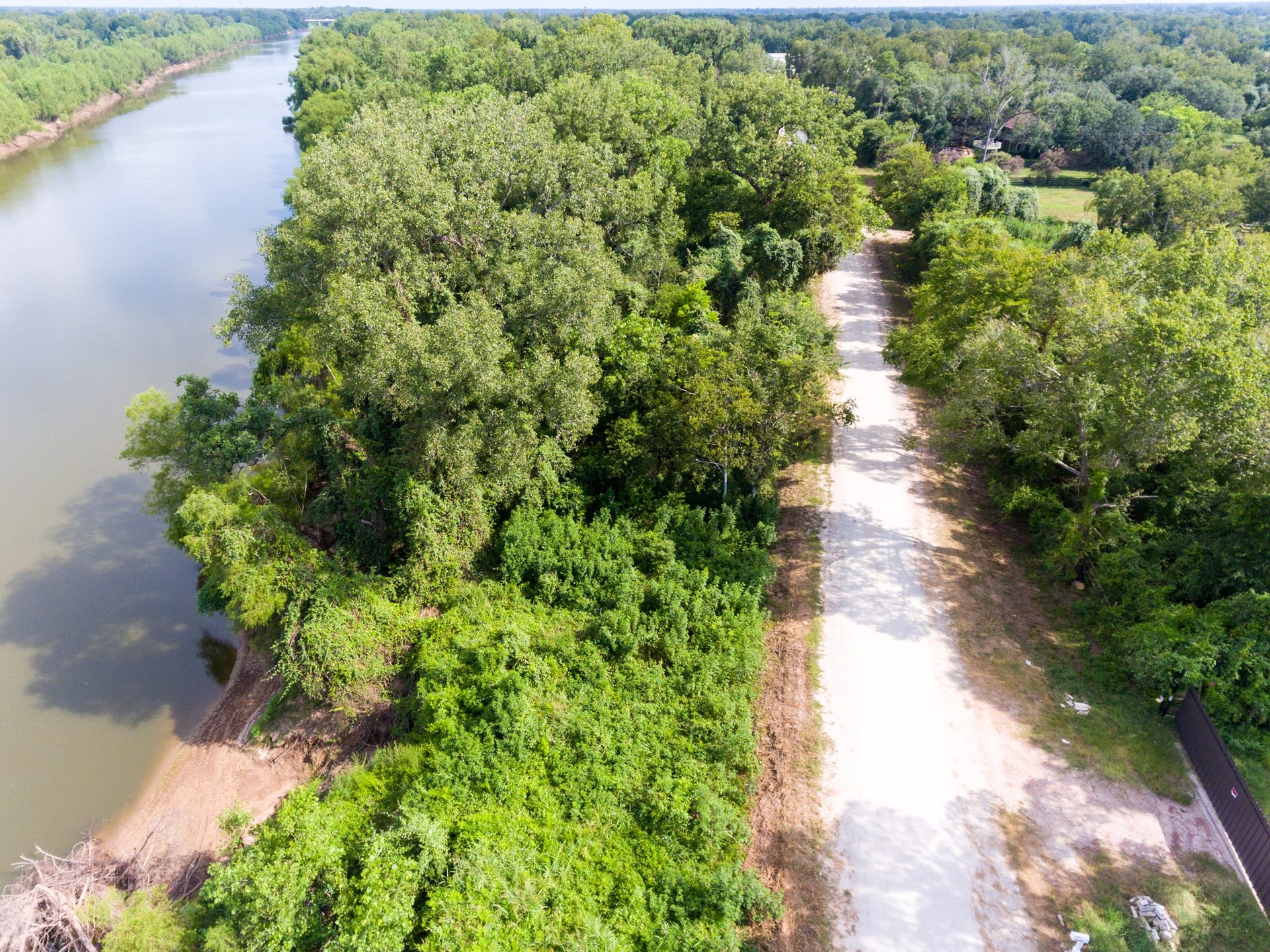 This aerial photo showcases a tranquil riverside location with a lush, tree-lined dirt road leading to a secluded area. Ideal for nature lovers seeking privacy and scenic views.