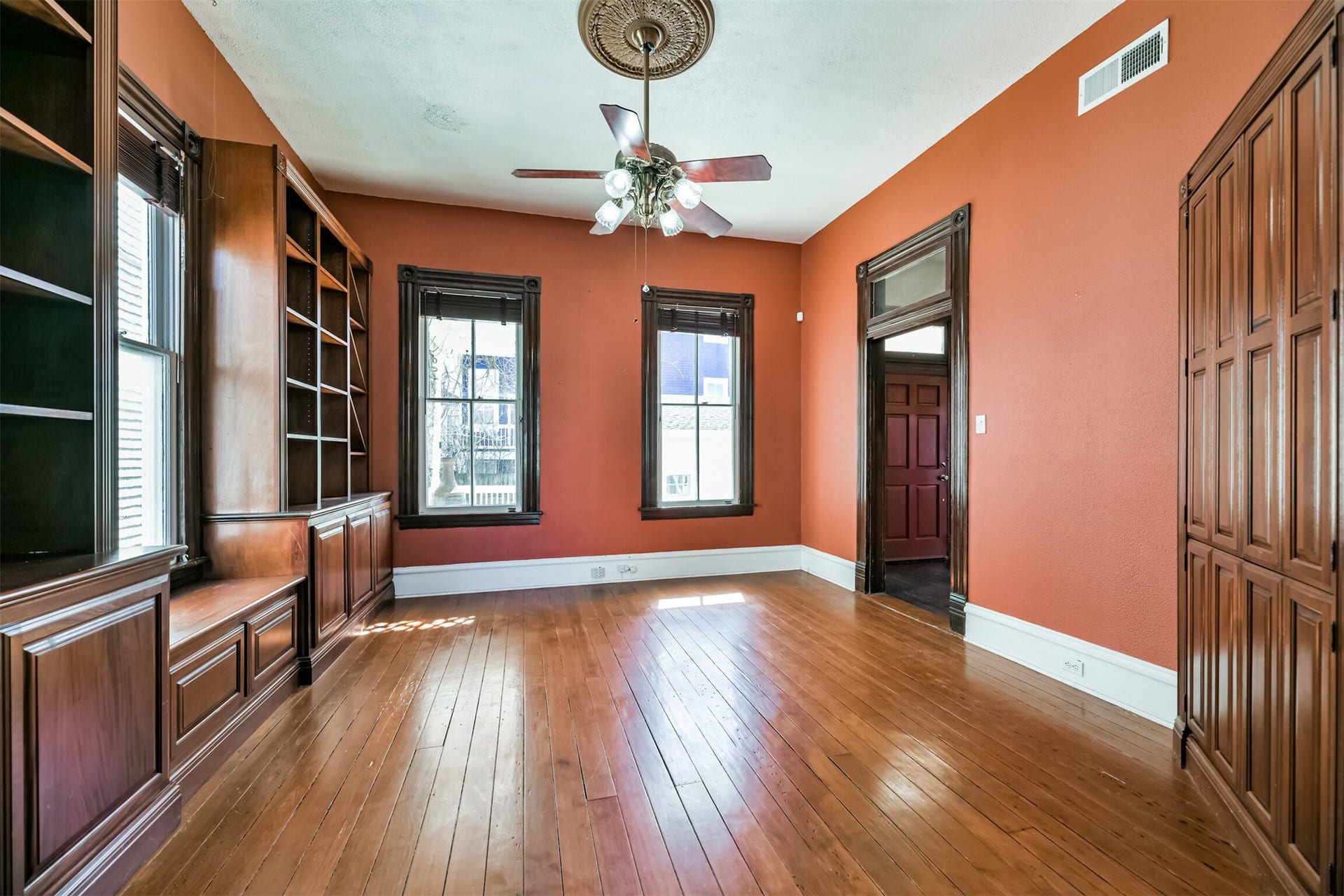 1927 Broadway Street, Galveston, TX 77550 An alternate view of the family room highlights the handsome long leaf pine wood flooring, ornate ceiling medallion with a lighted fan suspended from it, and beautifully cased windows and doors with an original transom window above the door.