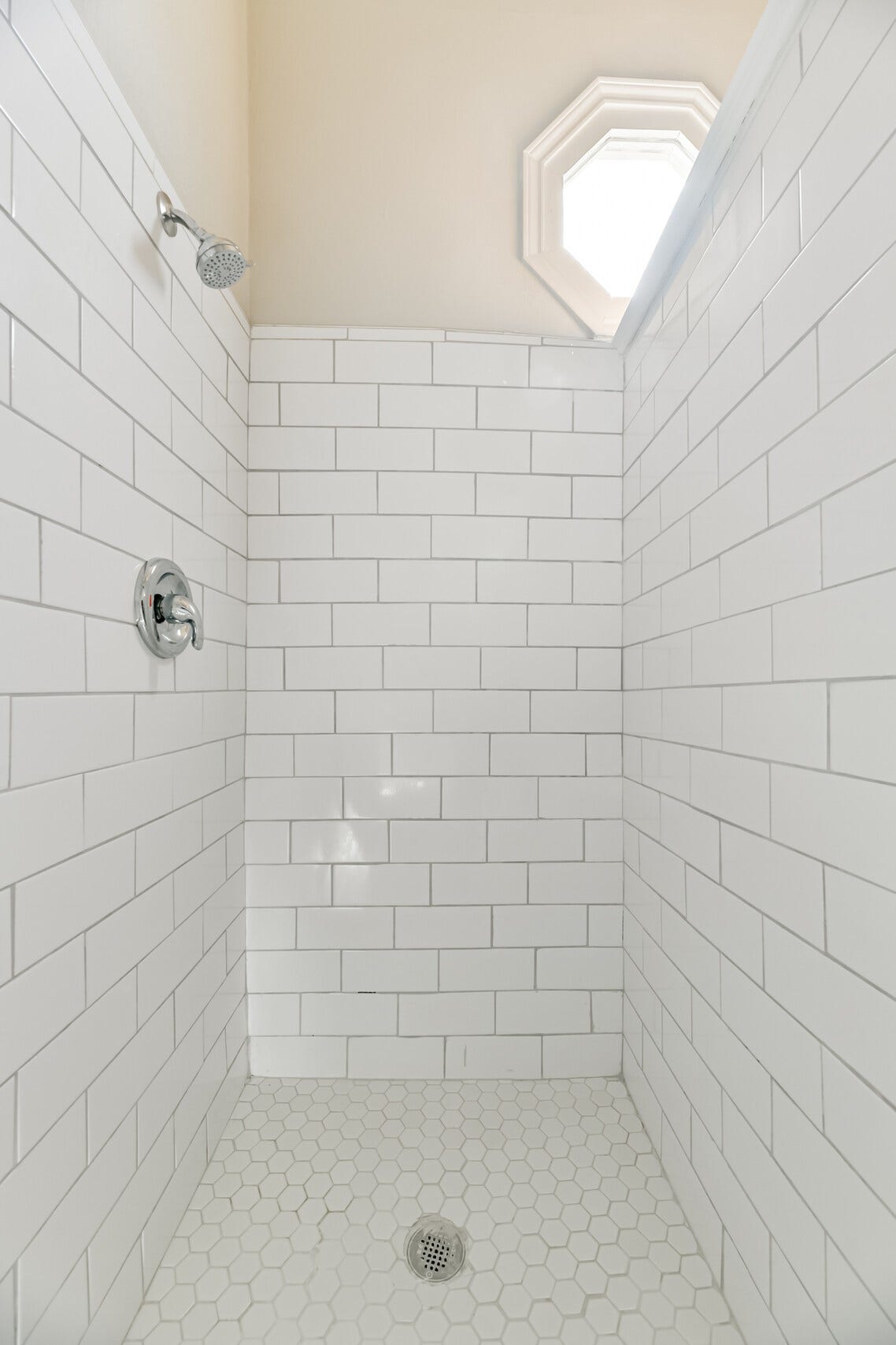 1927 Broadway Street, Galveston, TX 77550 The walk-in shower showcases a timeless subway tile finish that complements the hexagonal tile floors. A window above adds natural light to this bathroom.