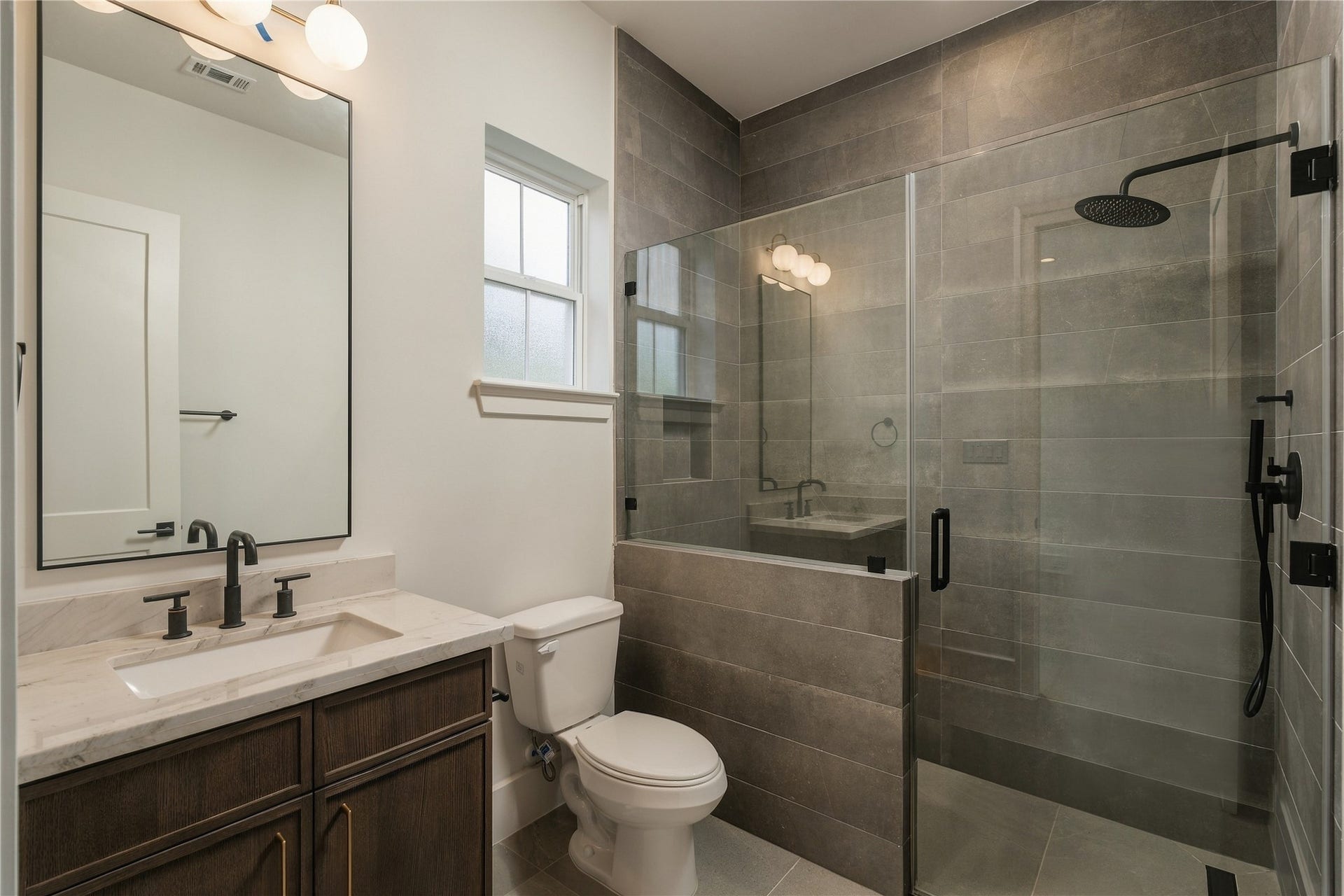 2107 McKean Drive, Houston, TX 77080 This secondary bath pairs Mount Blanc Quartzite with full-height designer tile and a frameless glass shower, creating a polished ensuite experience with finishes typically reserved for a primary suite.