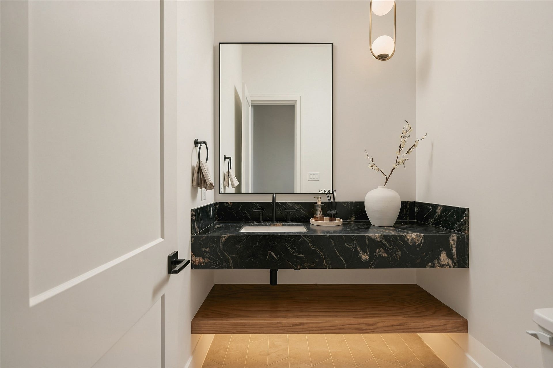 2107 McKean Drive, Houston, TX 77080 A powder room designed as its own moment, where a floating vanity wrapped in Titanium Quartzite brings drama and sculptural presence to the compact space. *WOOD SHELF COLOR MAY VARY, MODEL HOME PHOTO*