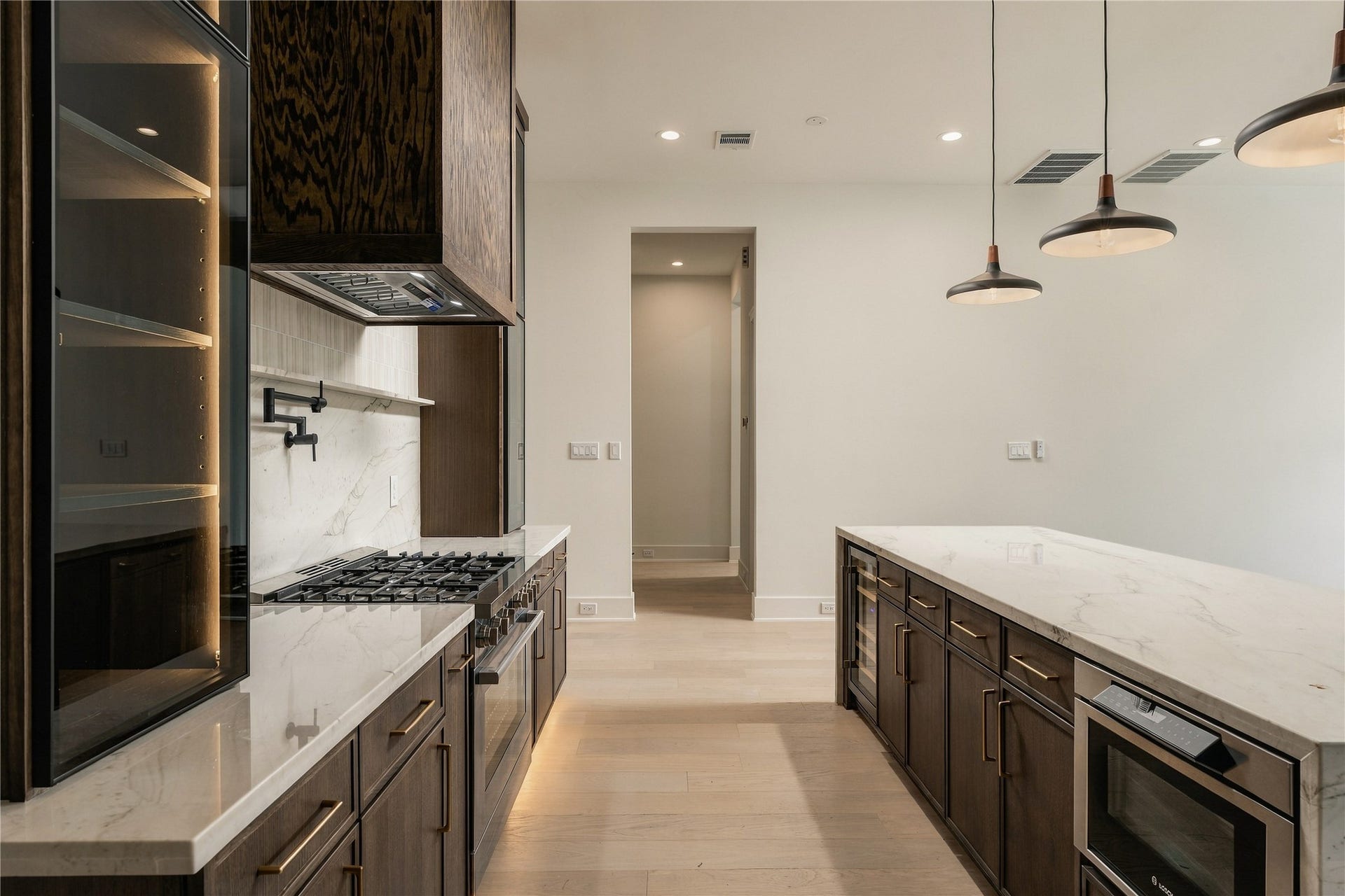 2107 McKean Drive, Houston, TX 77080 A dramatic perspective showcases the kitchens Midnight Glass Towers and illuminated cabinetry, creating a striking contrast against the warmth of the white oak finishes