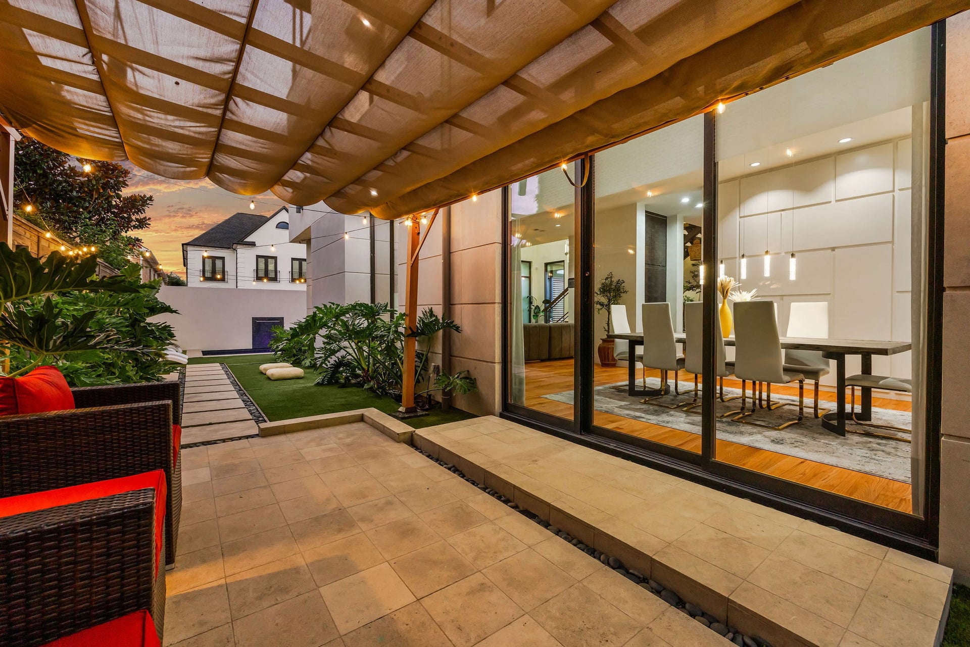 1310 Nantucket Drive, Houston, TX 77057 Experience seamless indoor-outdoor living with this elegant patio, featuring a shaded pergola and lush greenery, leading into a modern dining area through expansive glass doors.