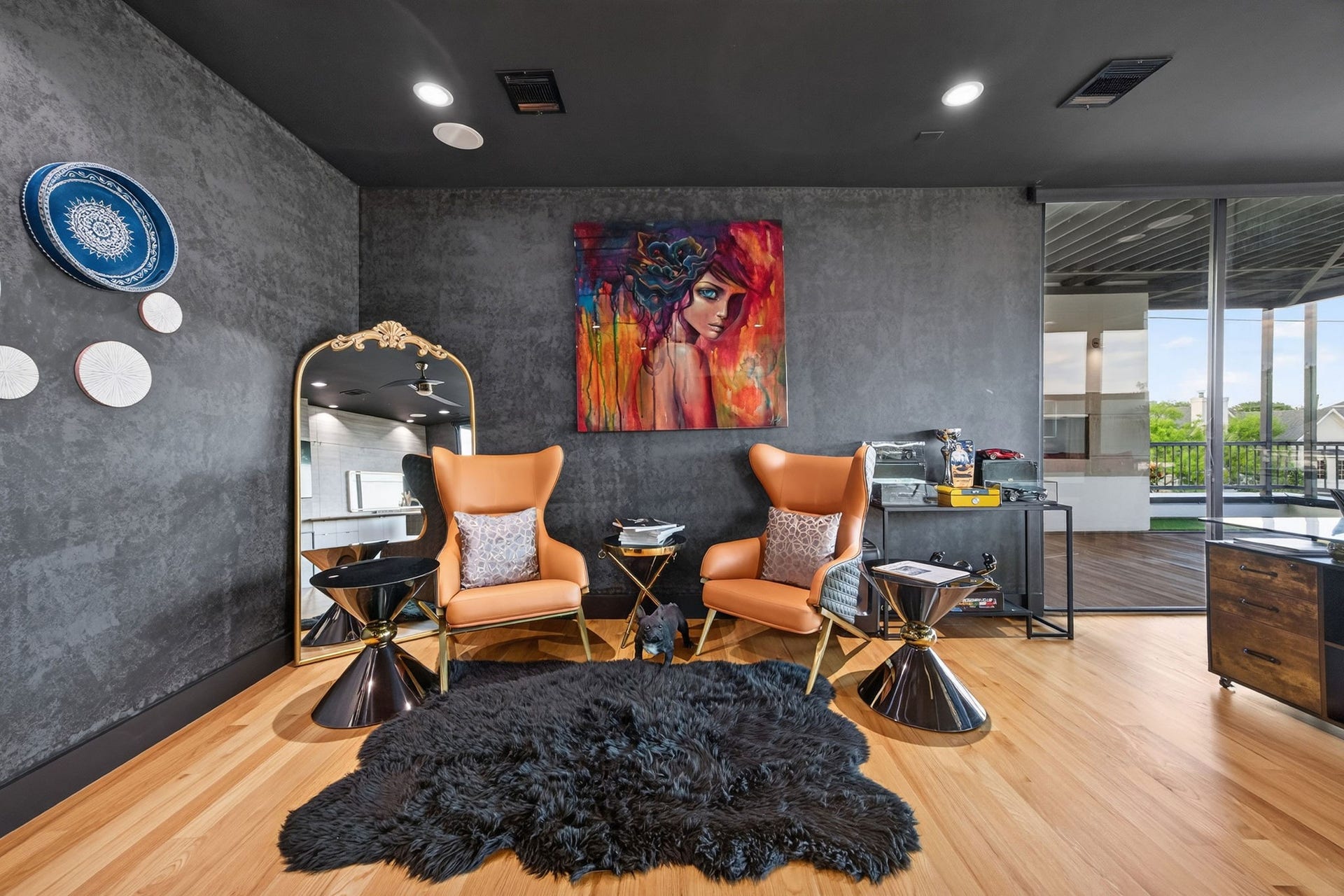 1310 Nantucket Drive, Houston, TX 77057 Stylish and modern living area with bold artwork, featuring sleek orange chairs and a cozy black rug against a textured gray wall, complemented by a large mirror and contemporary decor.