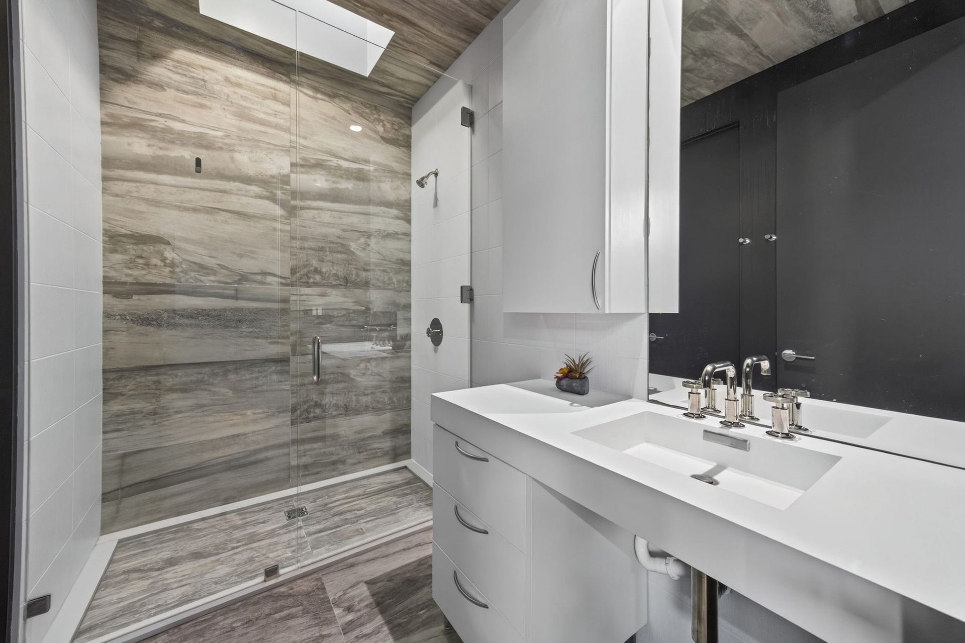 1310 Nantucket Drive, Houston, TX 77057 Sleek modern bathroom featuring a spacious walk-in shower with elegant stone tile, complemented by a chic double vanity with contemporary fixtures.