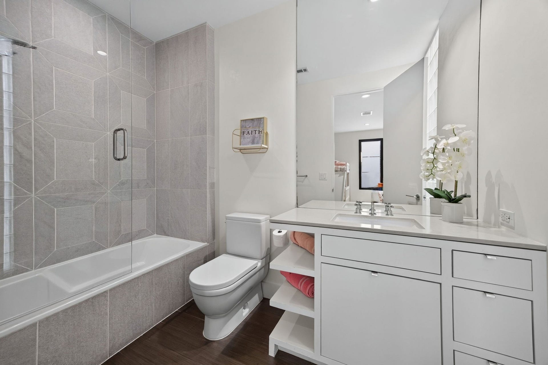 1310 Nantucket Drive, Houston, TX 77057 This bathroom features a spacious glass-enclosed tub and shower, elegant tile work, and a pristine white vanity with ample storage.