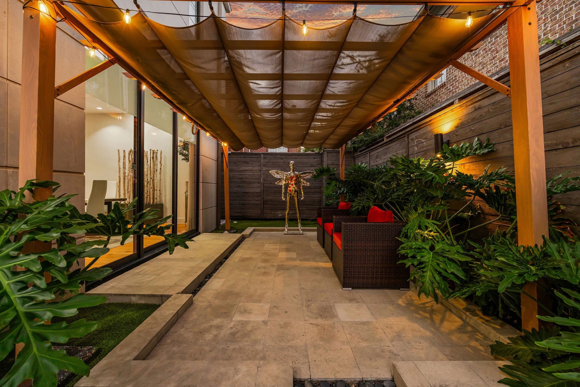 1310 Nantucket Drive, Houston, TX 77057 Charming outdoor patio with a cozy seating area under a stylish pergola, surrounded by lush greenery and ambient lighting.