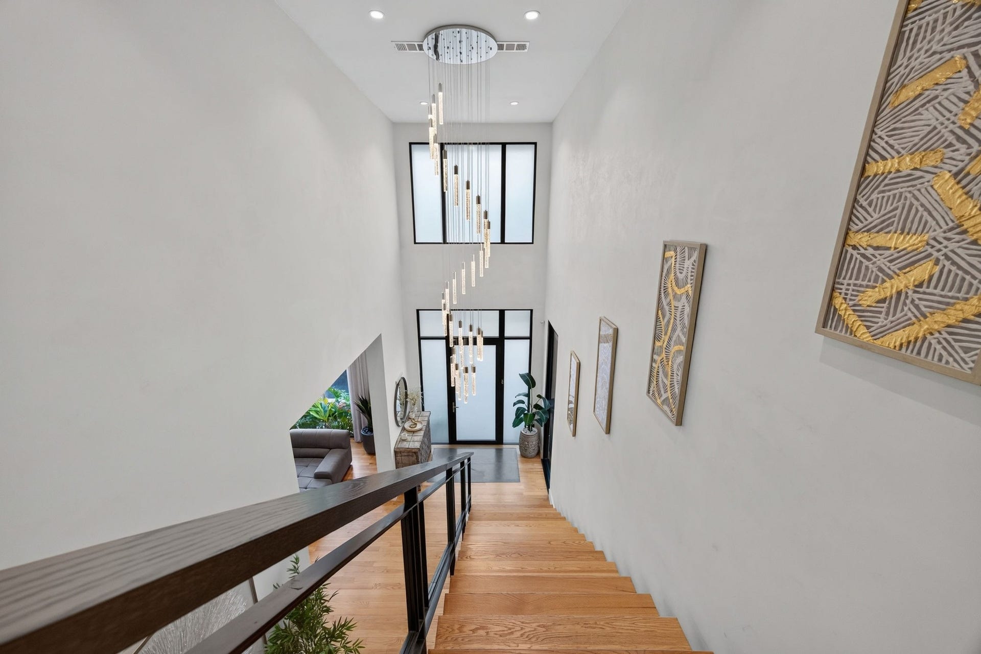 1310 Nantucket Drive, Houston, TX 77057 Elegant staircase featuring sleek wooden steps and a striking modern chandelier, complemented by large windows that flood the space with natural light.