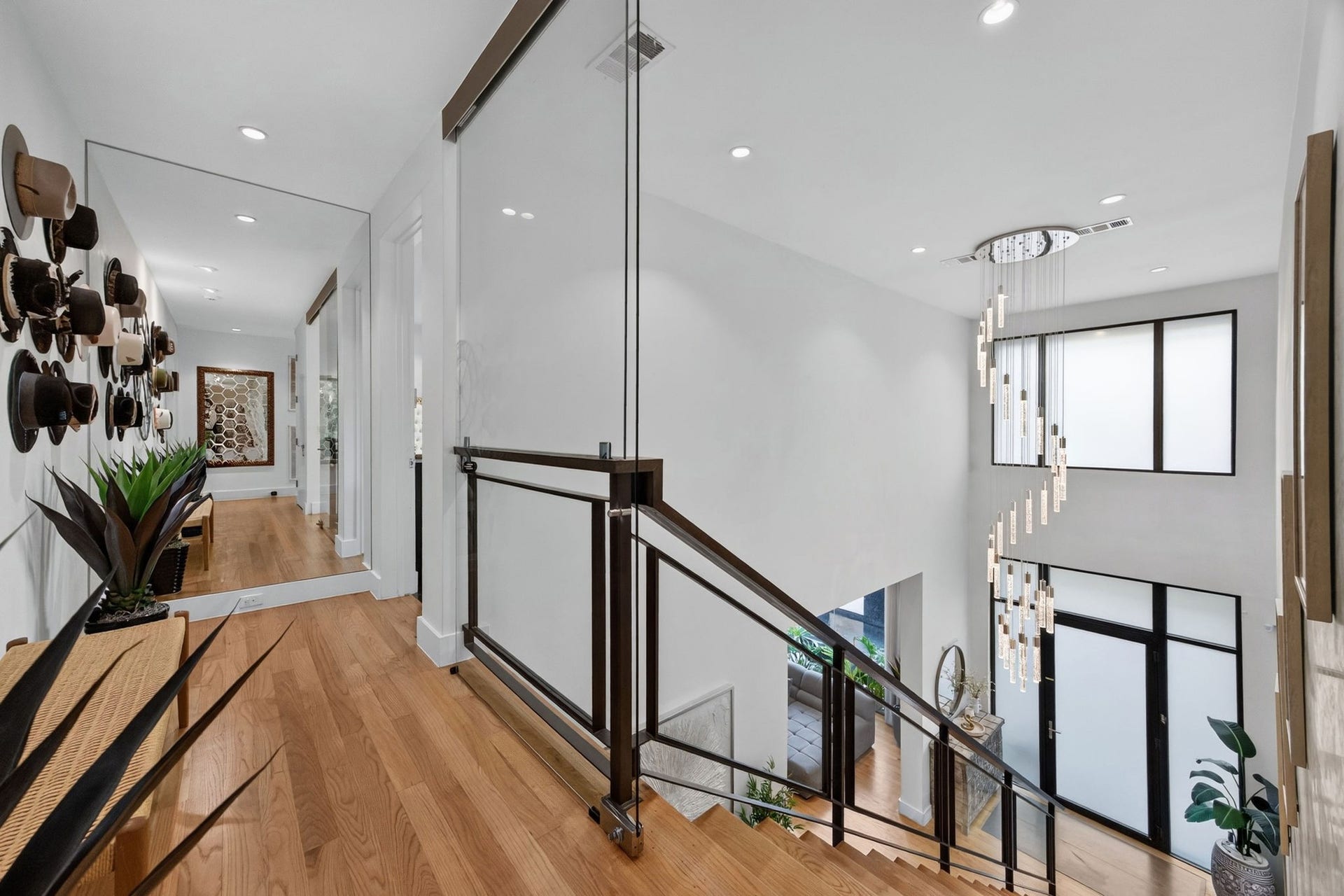 1310 Nantucket Drive, Houston, TX 77057 Inviting hallway with sleek hardwood floors, accentuated by a stylish hat display and contemporary lighting, leading to a bright, open staircase with large windows.