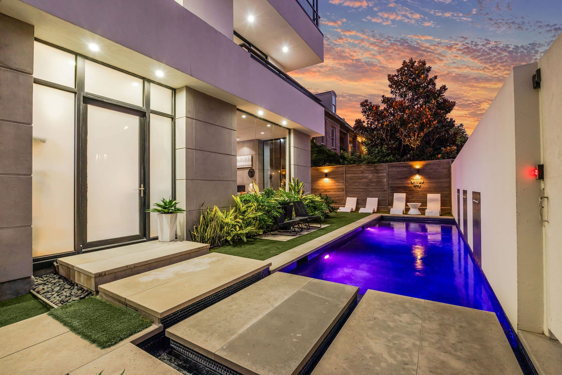 1310 Nantucket Drive, Houston, TX 77057 Luxurious modern outdoor space featuring a sleek pool with vibrant lighting, surrounded by elegant lounge chairs and lush greenery, perfect for relaxing and entertaining.