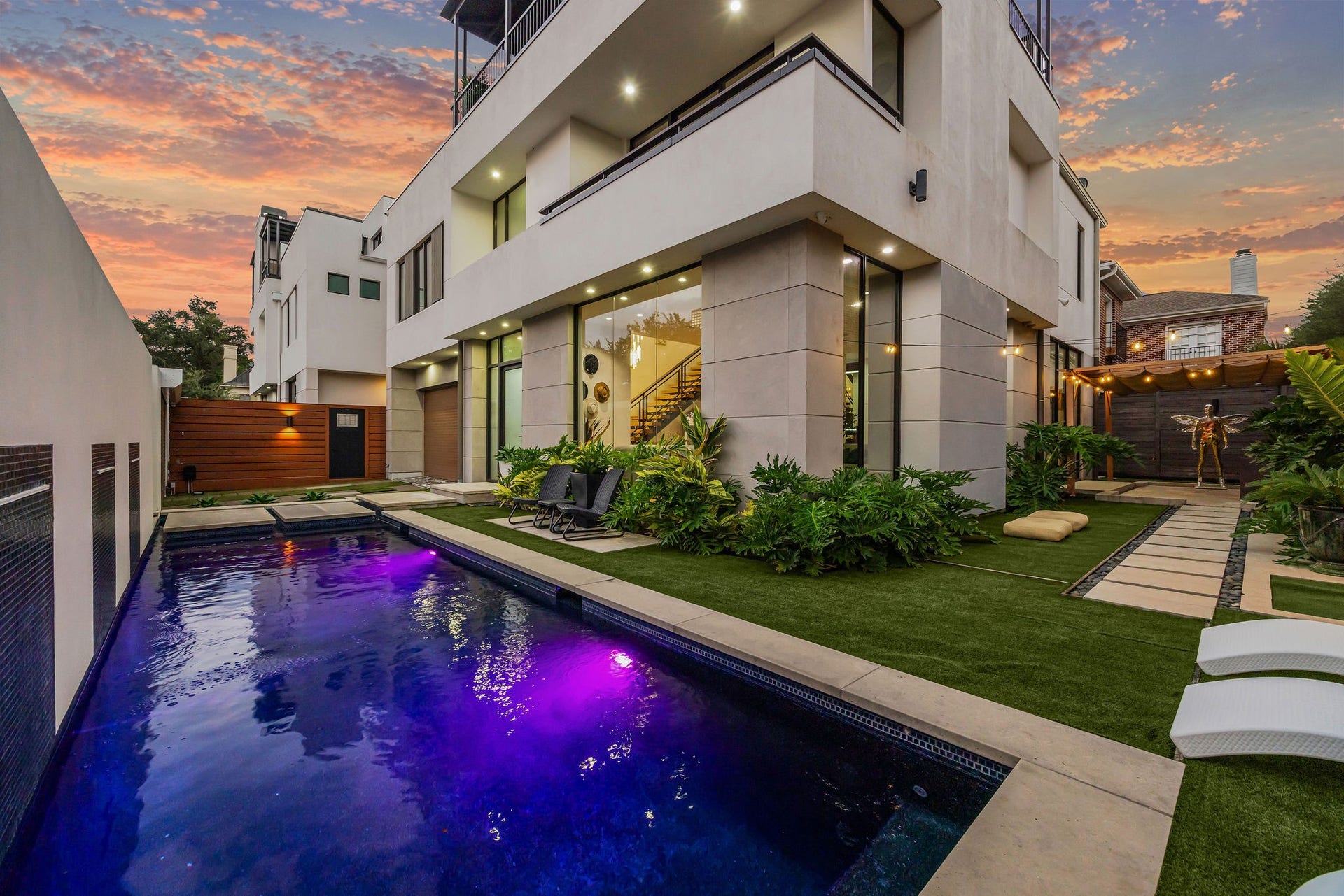 1310 Nantucket Drive, Houston, TX 77057 Modern luxury home featuring a sleek pool with vibrant lighting, surrounded by lush landscaping and a stylish outdoor lounge area, perfect for entertaining.
